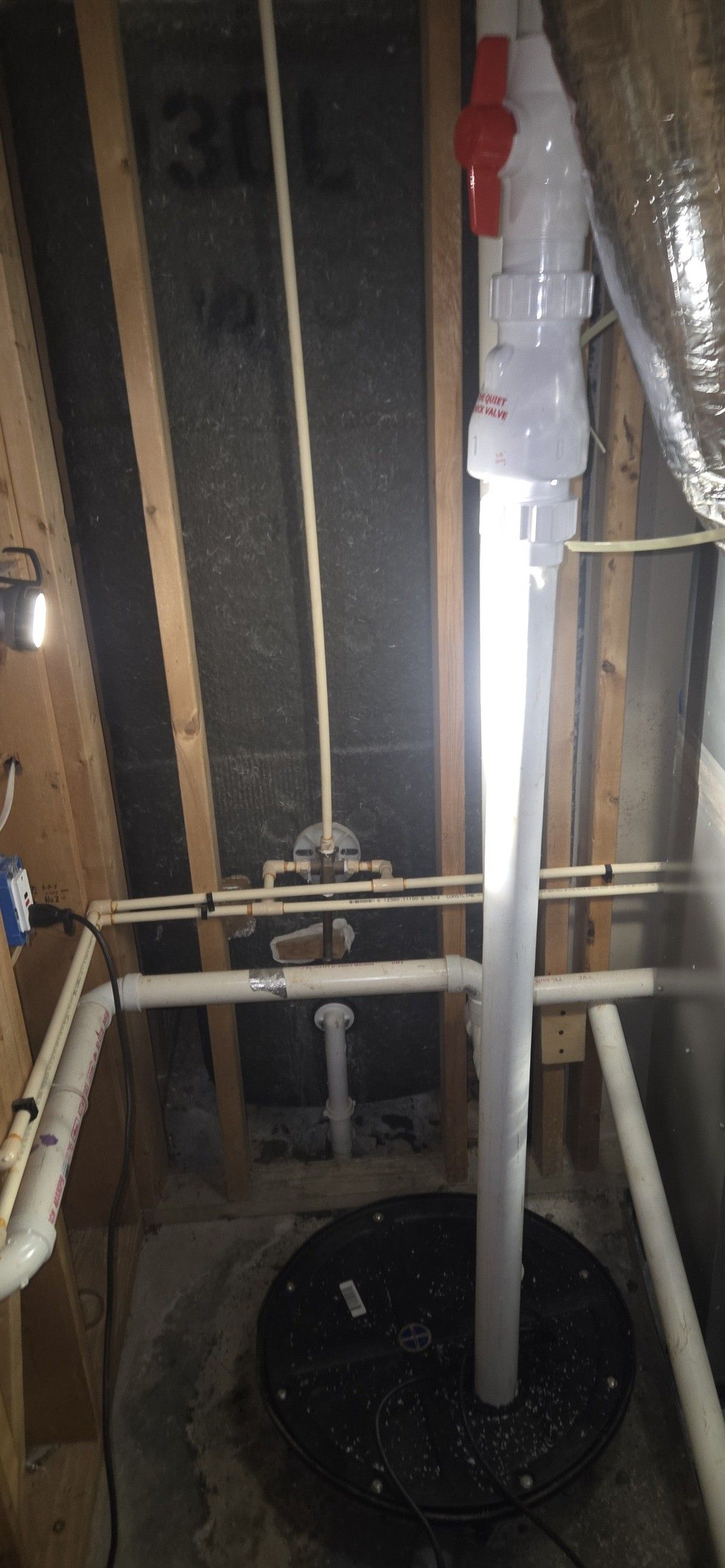 Sump pump installation in a basement with exposed wooden framing and piping.