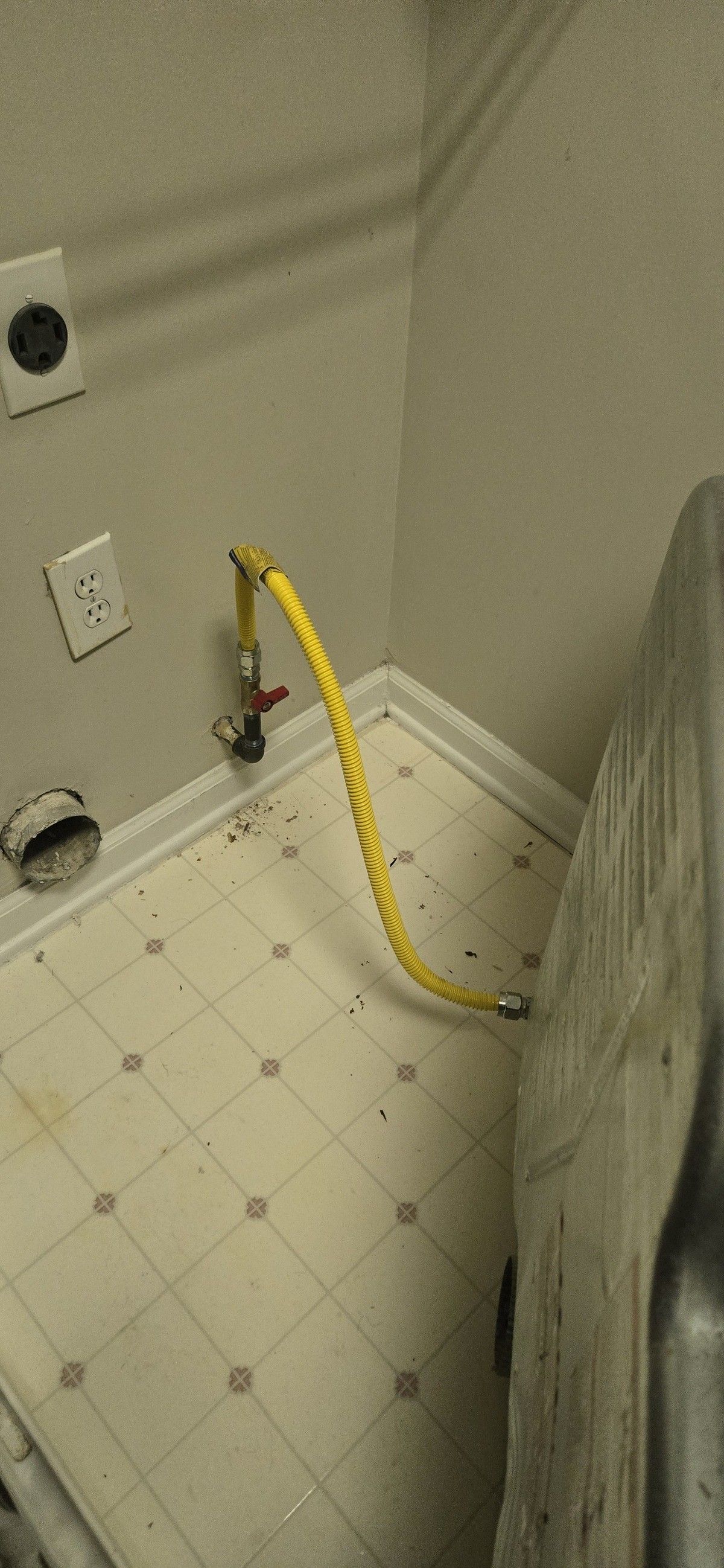 Yellow gas line and valve on a wall with electrical outlets and an exhaust vent in a laundry room.