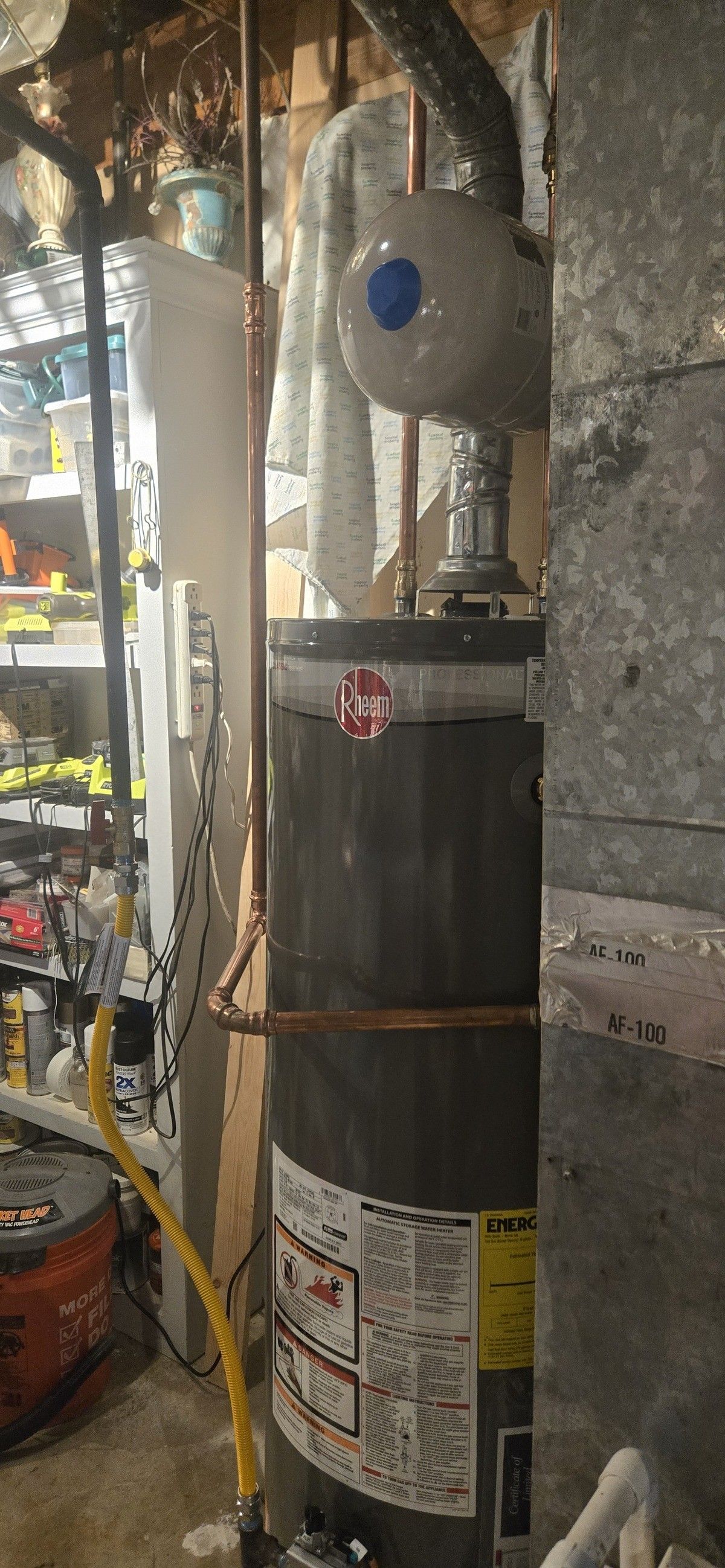 A water heater in a basement. Copper pipes run to it. A yellow wire is near the base.