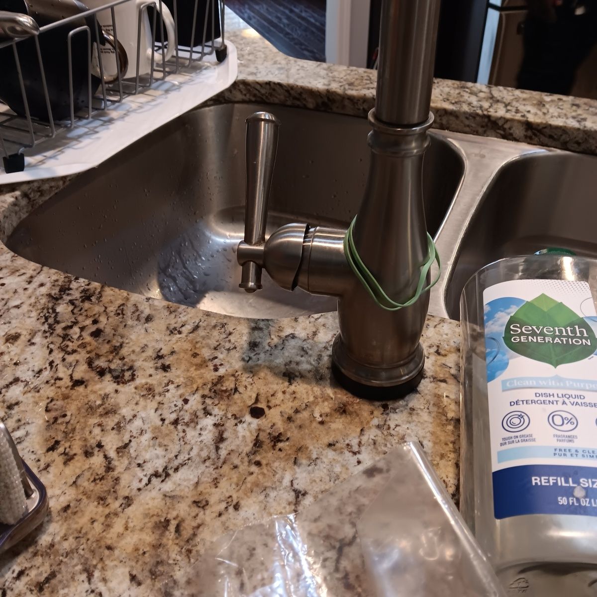 Kitchen sink with faucet, granite countertop, and soap dispenser. Dish rack on the left.