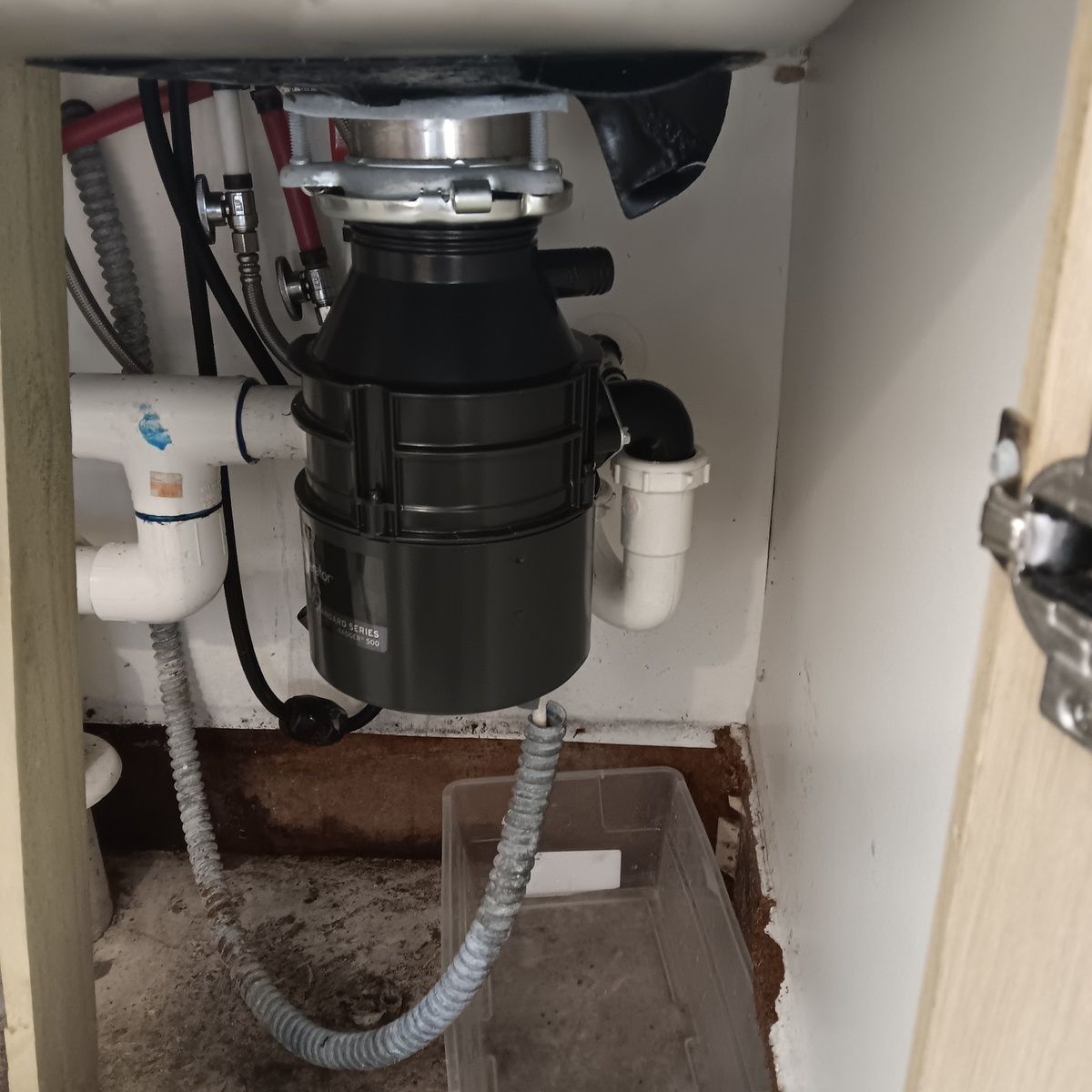 Garbage disposal unit installed under a kitchen sink with connected plumbing and drain pipe.