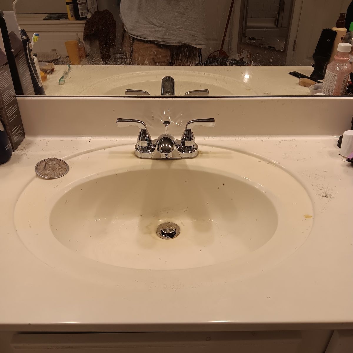Bathroom sink with chrome faucet and oval basin. Beige countertop and mirror.