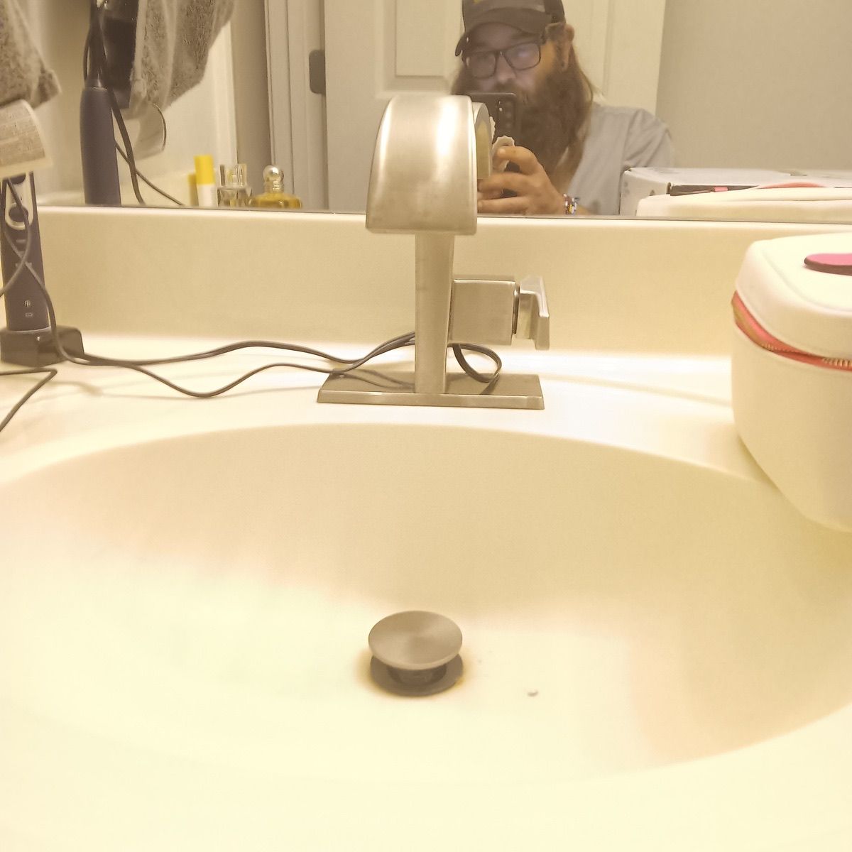 Bathroom sink with chrome faucet; person in mirror taking a photo.