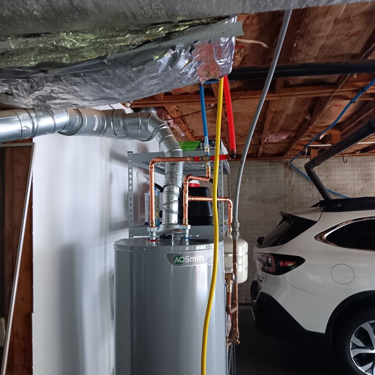 Water heater with copper pipes in a garage, next to a white SUV.