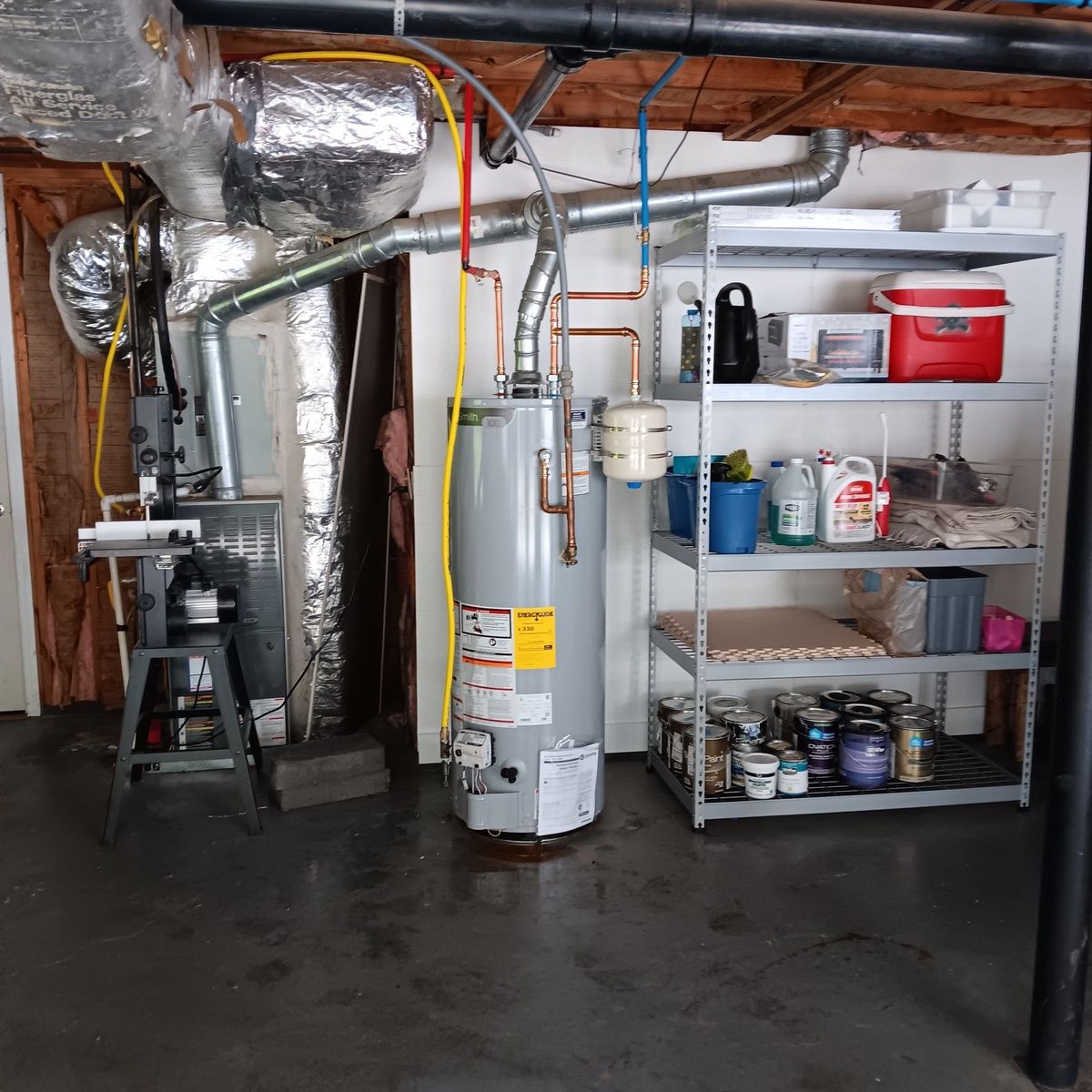 Basement with water heater, HVAC, shelves holding supplies. Pipes, ducts, gray floor.