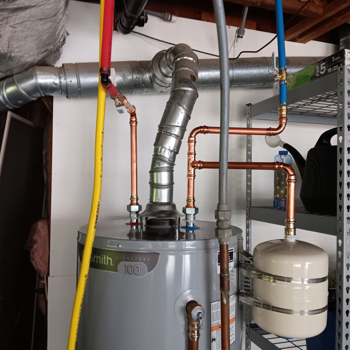 Water heater with connected copper pipes and ventilation ducting against a wall, with an expansion tank.