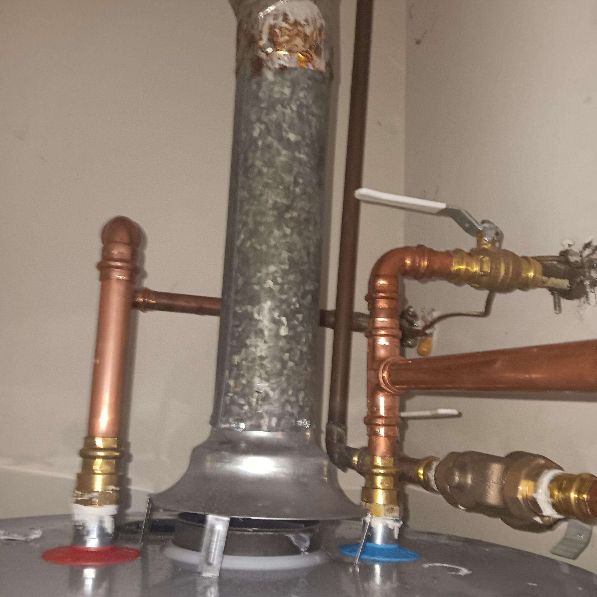 Water heater with copper pipes, a metal vent, and valves.