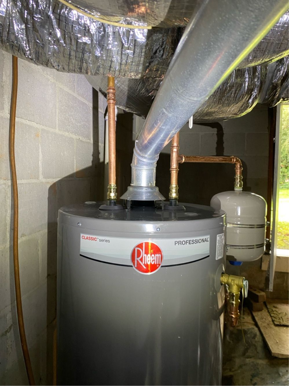 Rheem water heater with copper pipes, venting, and an expansion tank in a basement setting.
