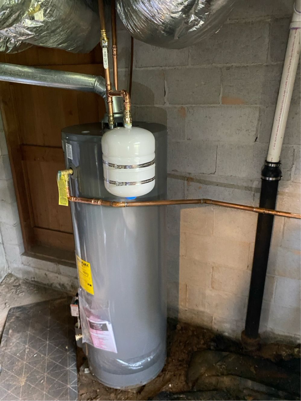 Water heater with an expansion tank, pipes, and ductwork in a basement setting.
