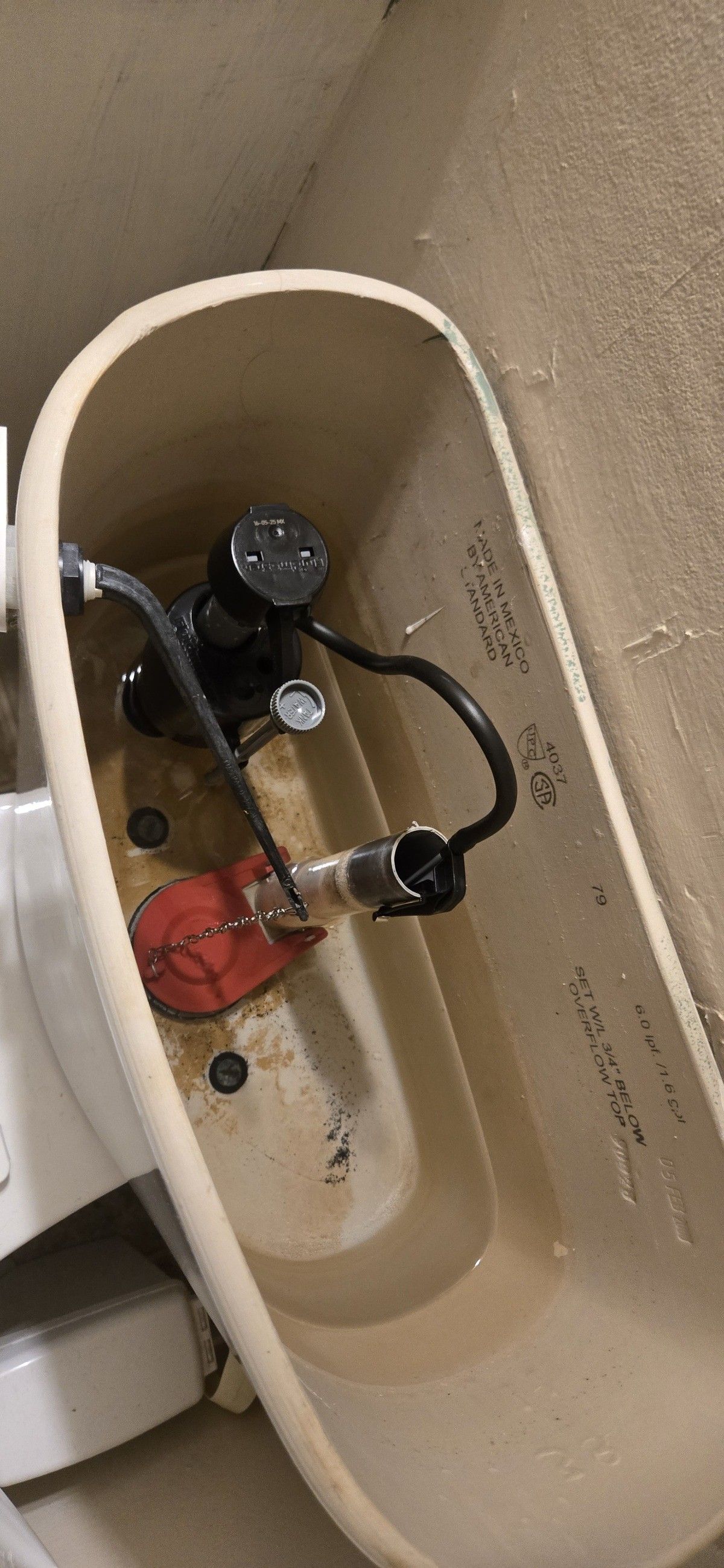 Inside view of a toilet tank, showing the water filling mechanism, hoses, and red float.