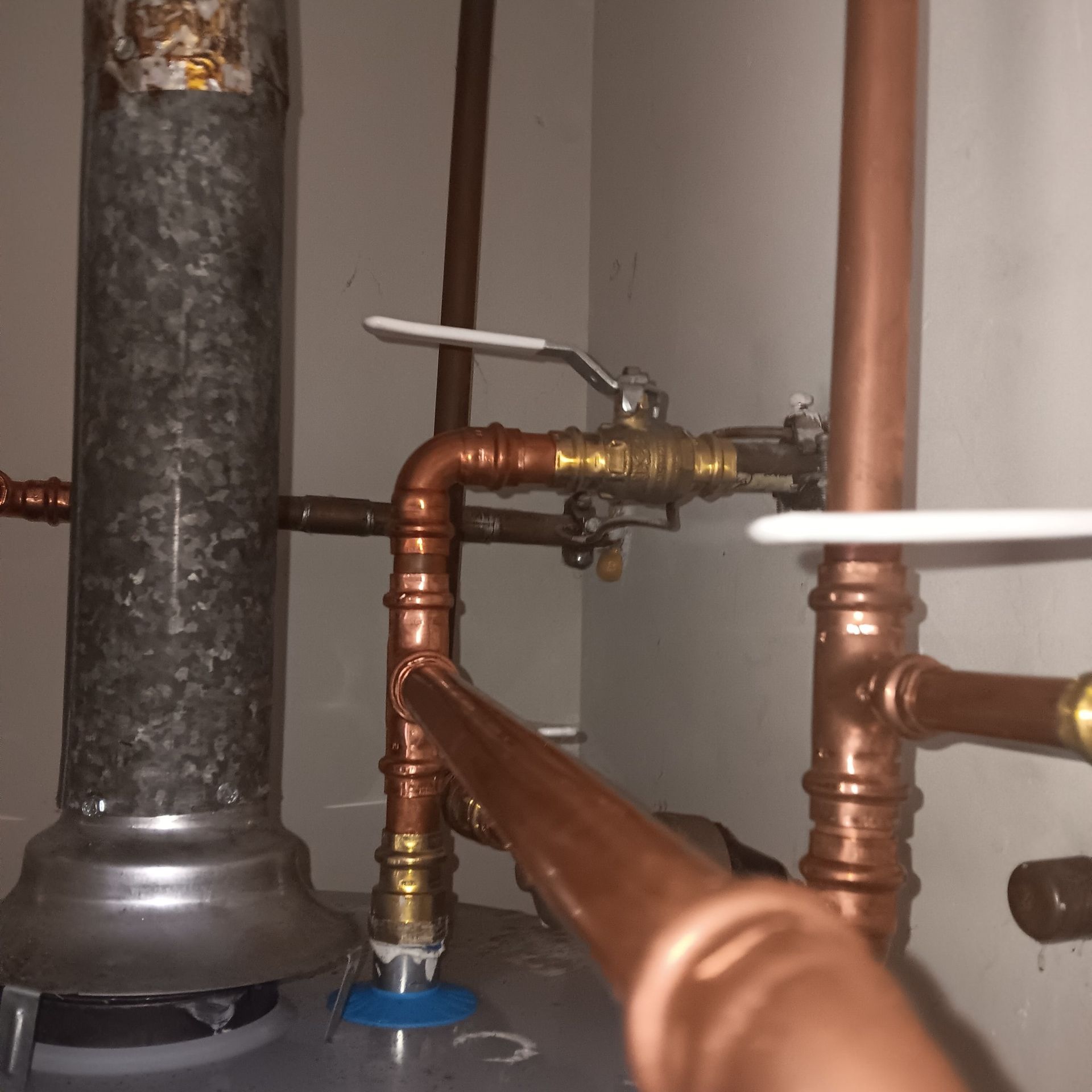 Copper pipes and valves connected to a water heater in a utility closet.