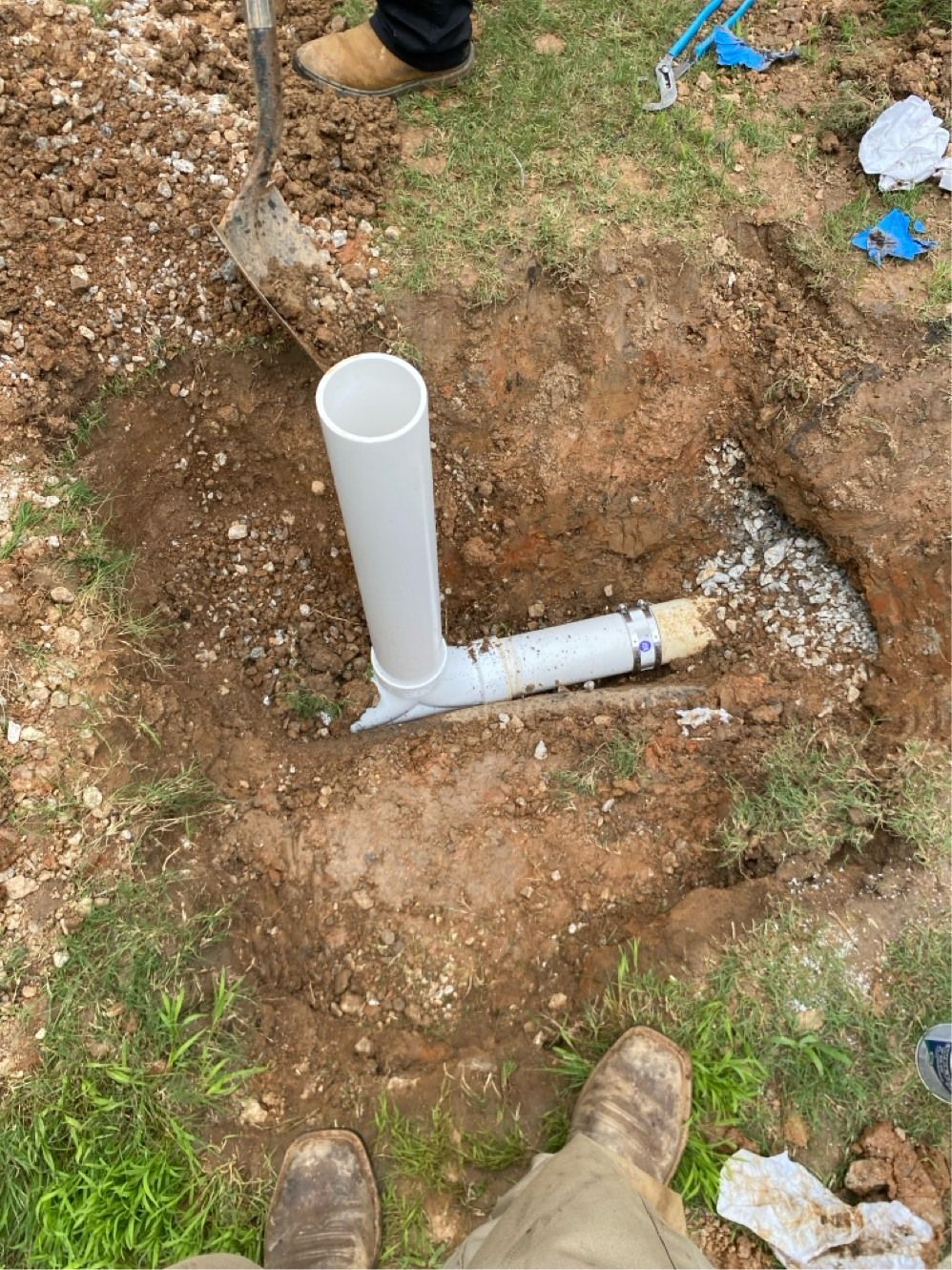 PVC pipe installation in dirt with a person holding a shovel, surrounded by grass.