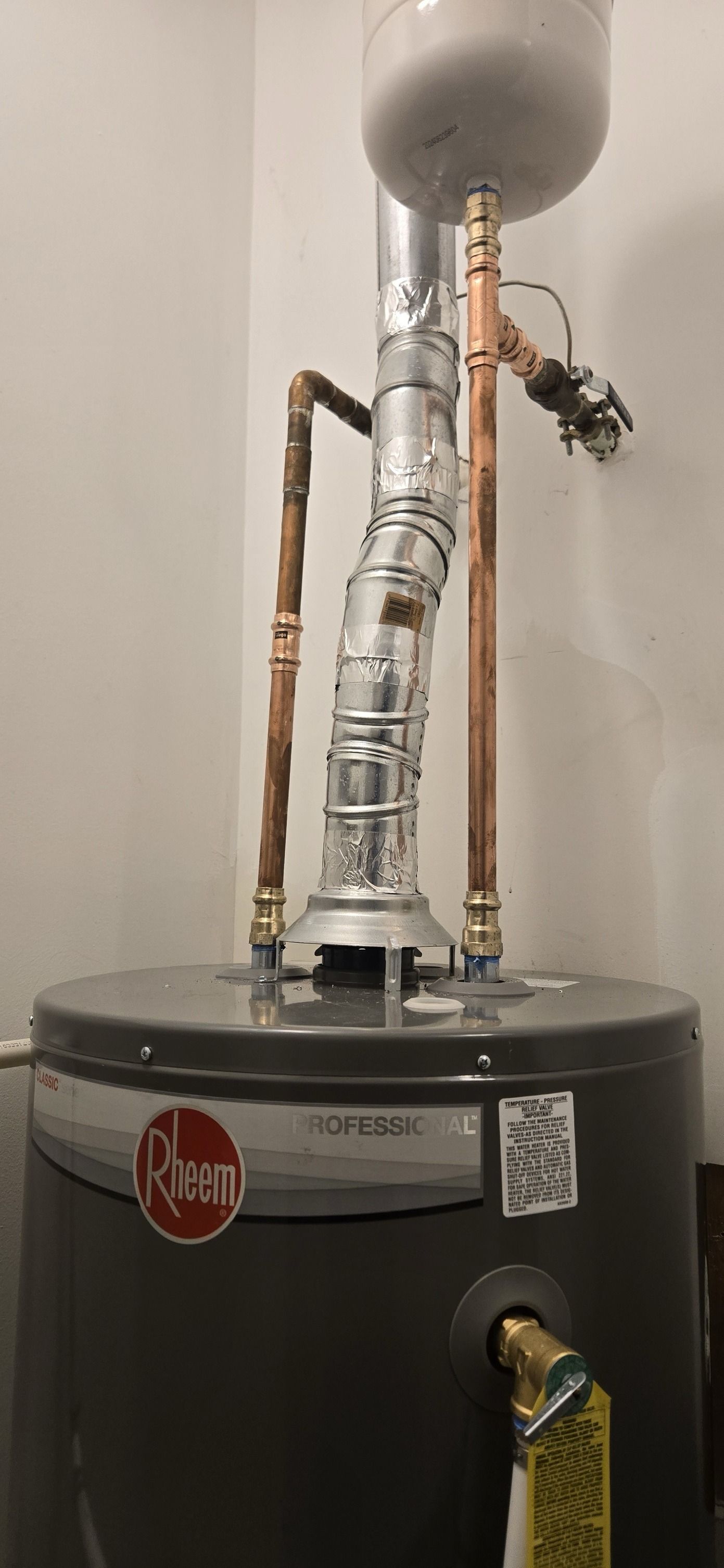 Rheem hot water heater with copper pipes, a silver flue, and an expansion tank.