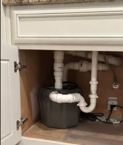 A gray basin with white pipes under a bathroom sink inside a white cabinet.