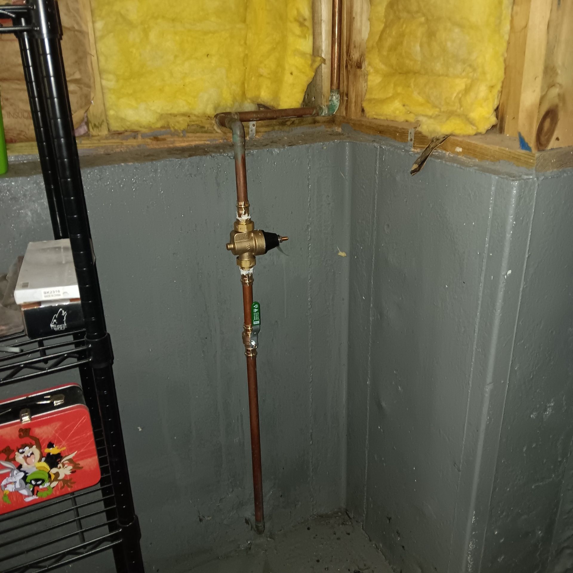 Copper pipes with a brass valve and a green handle in a basement corner.