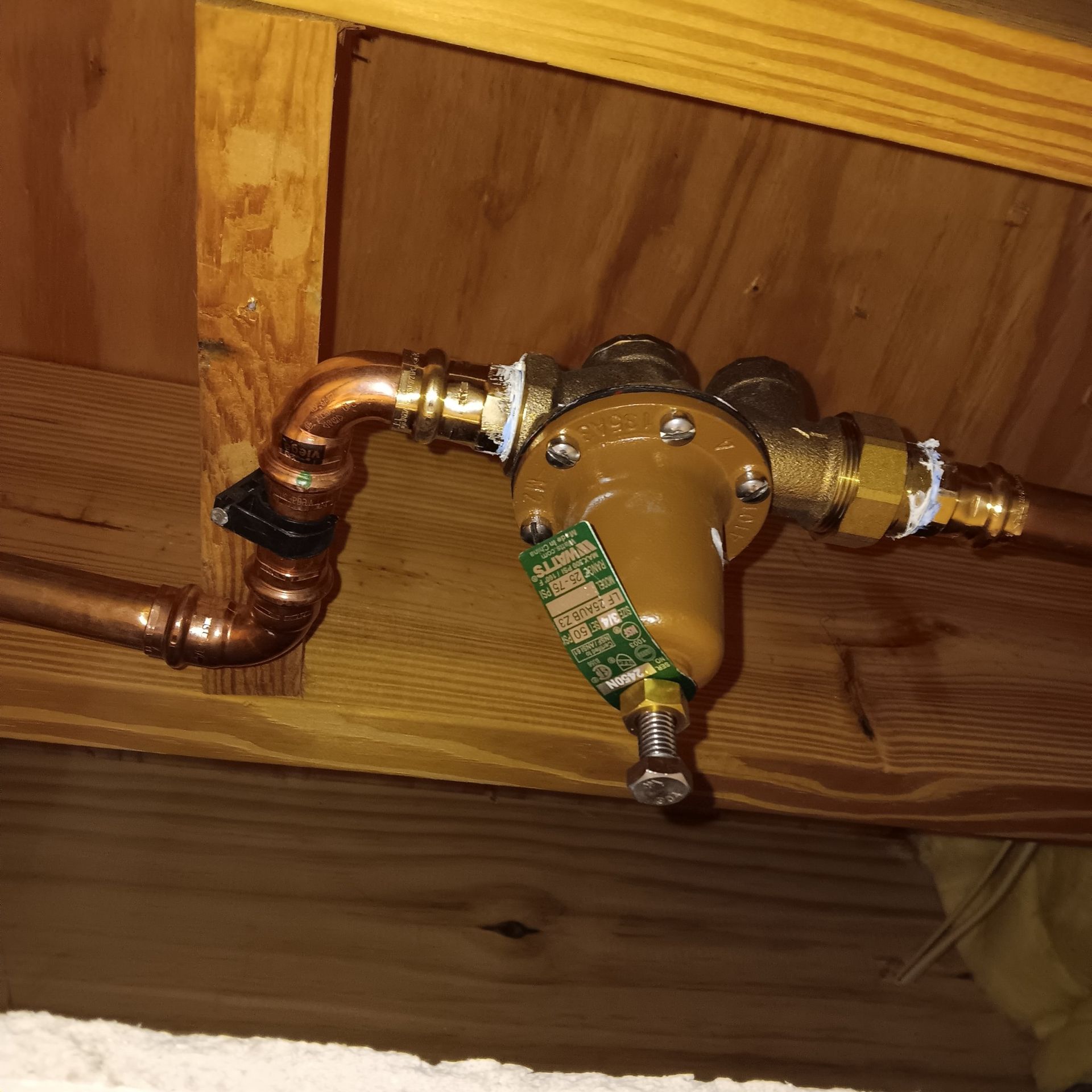 Copper pipes and a brown pressure reducing valve installed on a wooden structure.