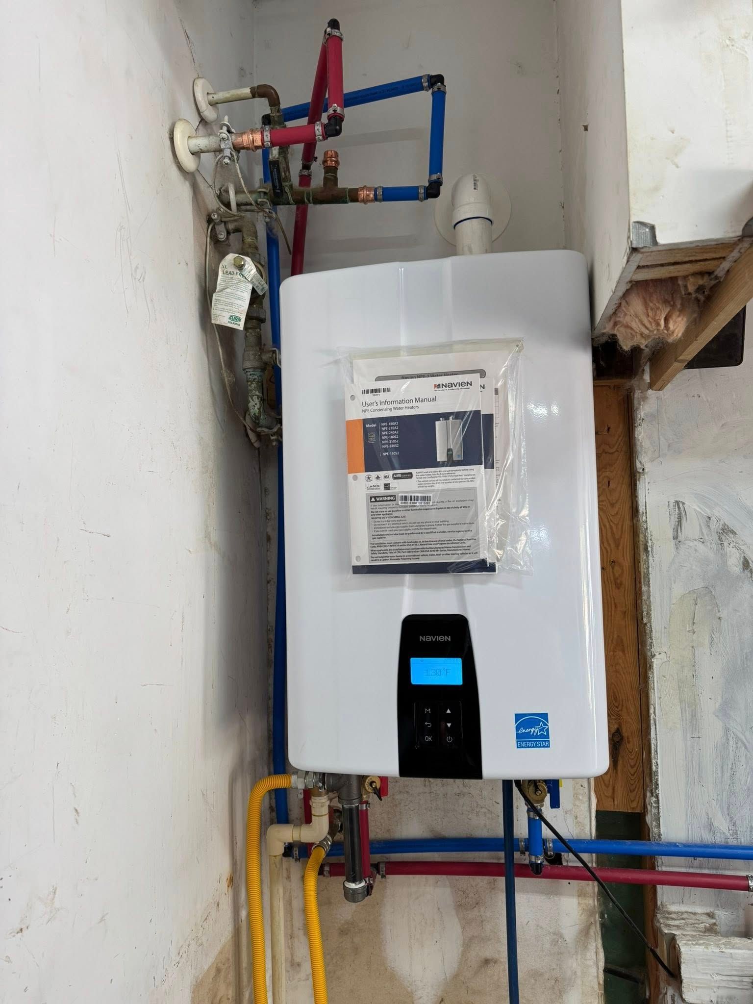 White tankless water heater mounted on a wall with connected blue, red, and yellow pipes.
