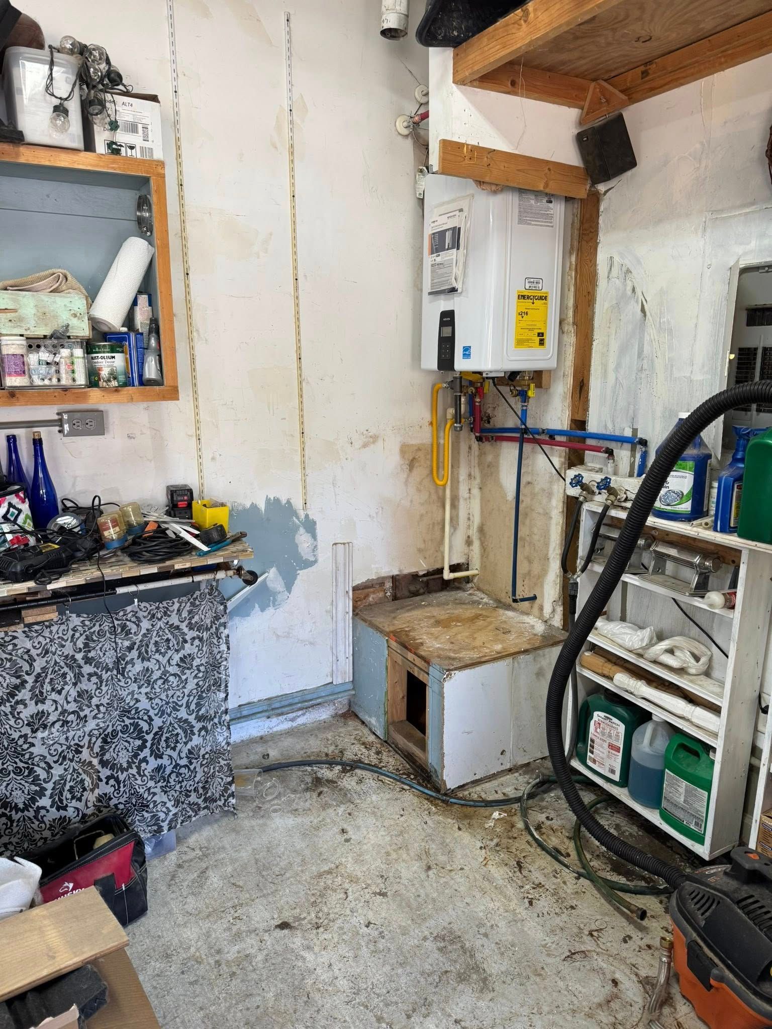Garage interior with water heater, storage, and exposed pipes on a dirty concrete floor.