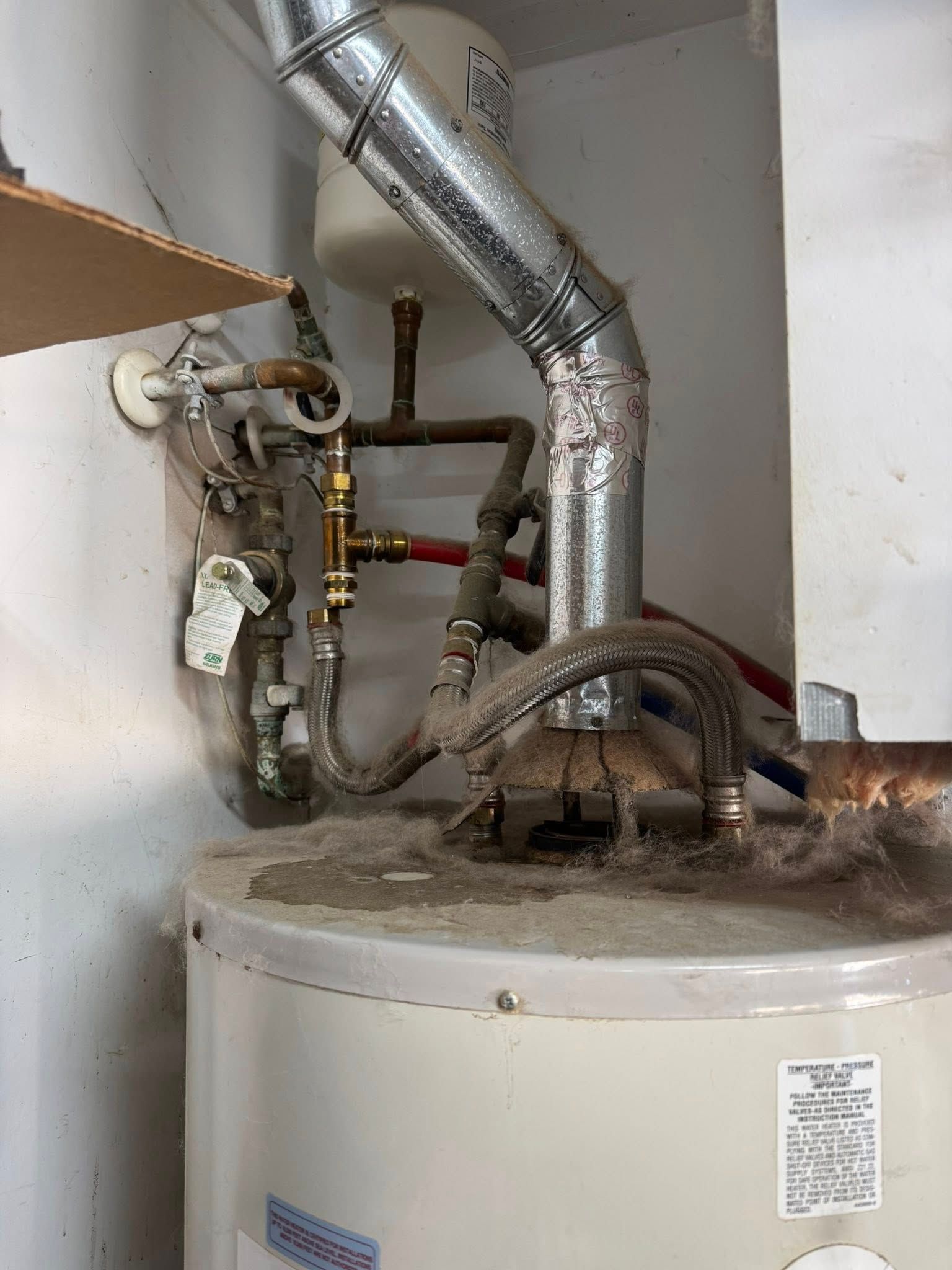 Water heater with connected pipes and vent in a utility room.
