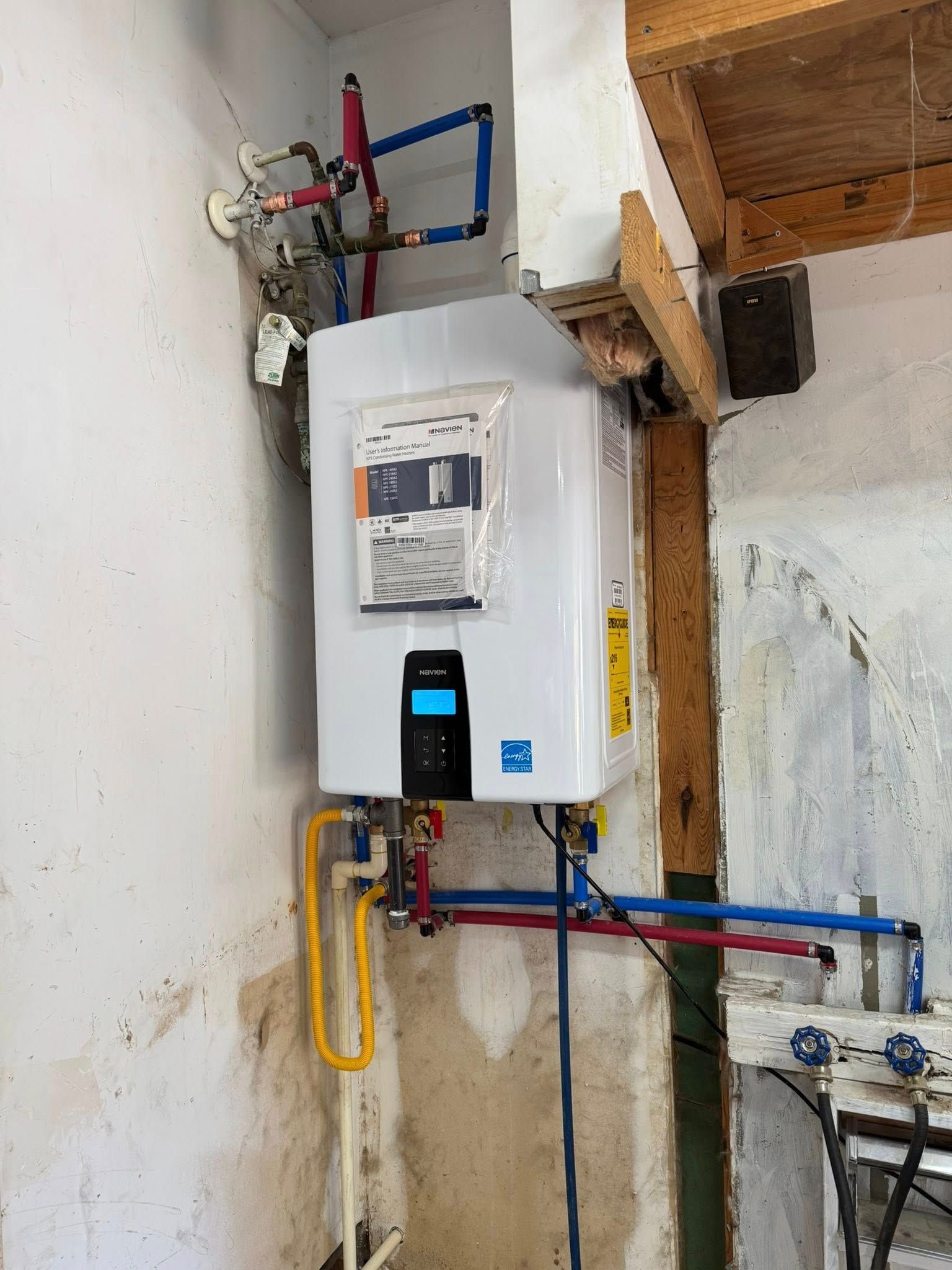 Tankless water heater installed on a wall with various pipes connected, and a control panel.
