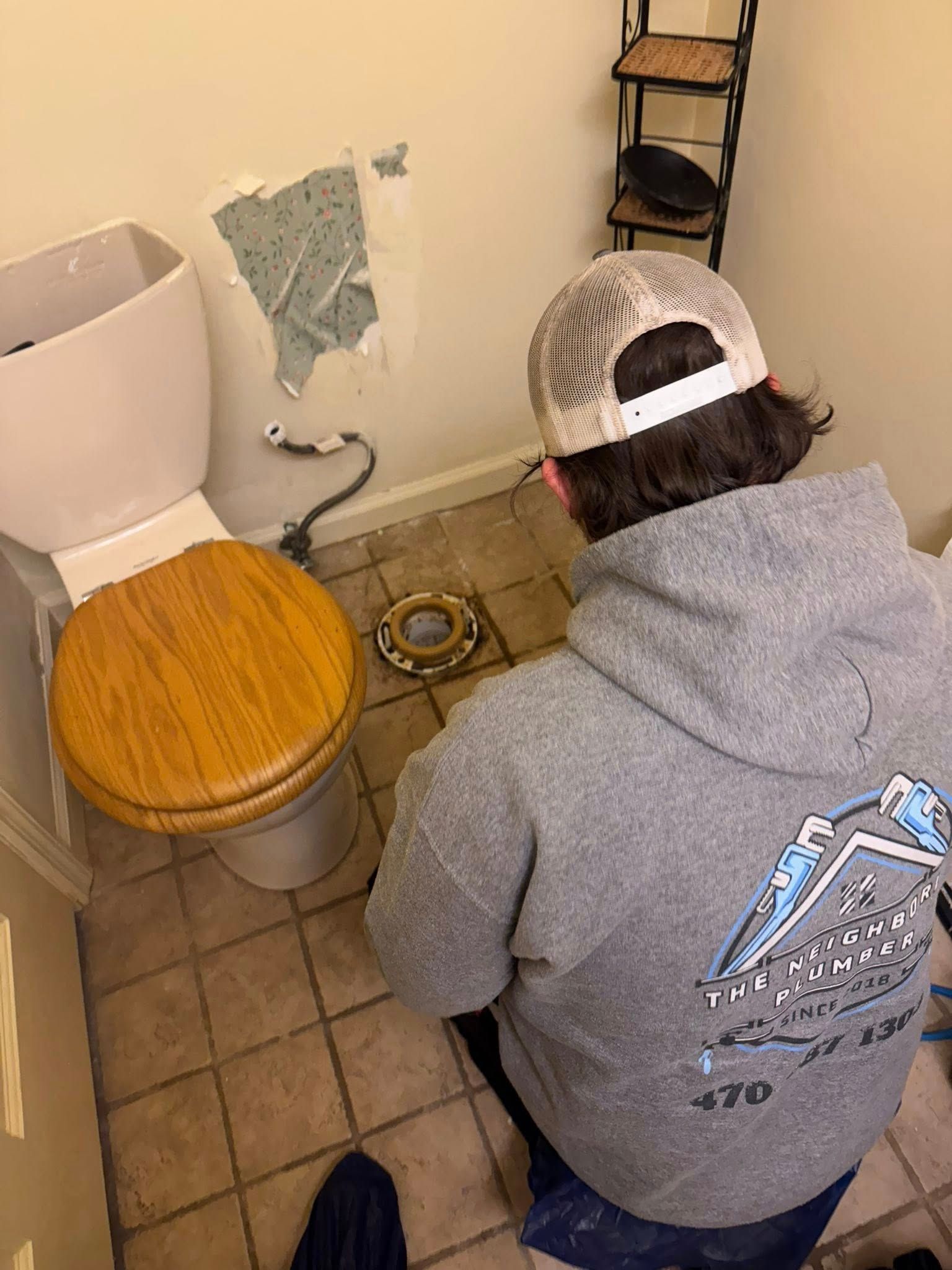 Person in a gray hoodie working on a toilet, with the toilet seat up, in a bathroom.