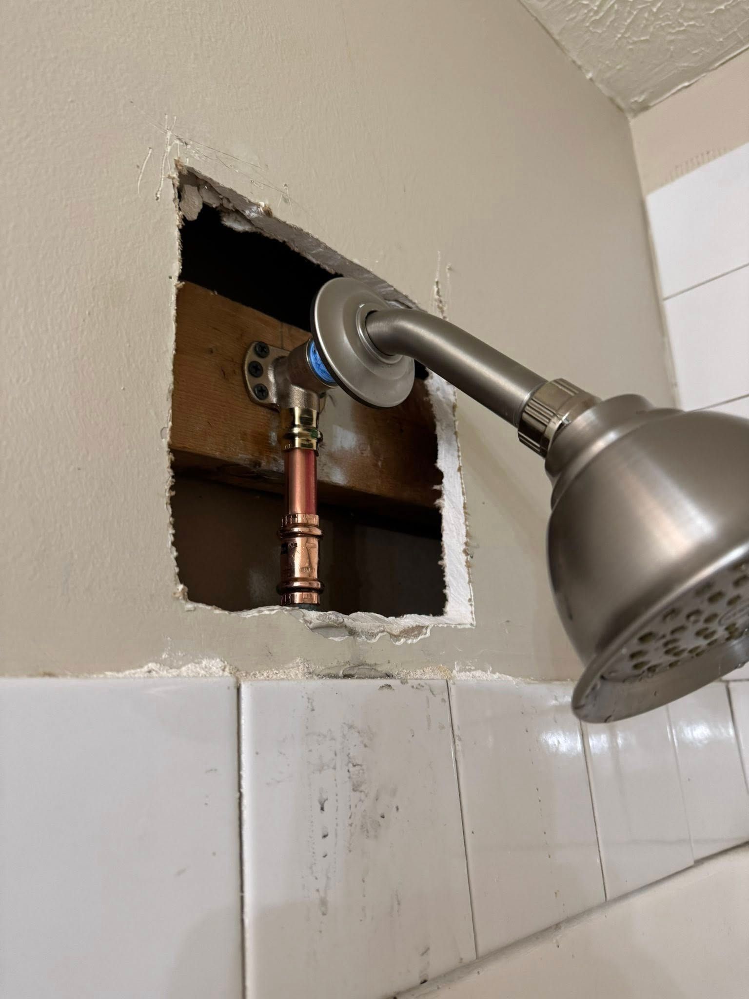 Showerhead and plumbing exposed in a wall opening, showing copper pipes and a partially installed shower arm.