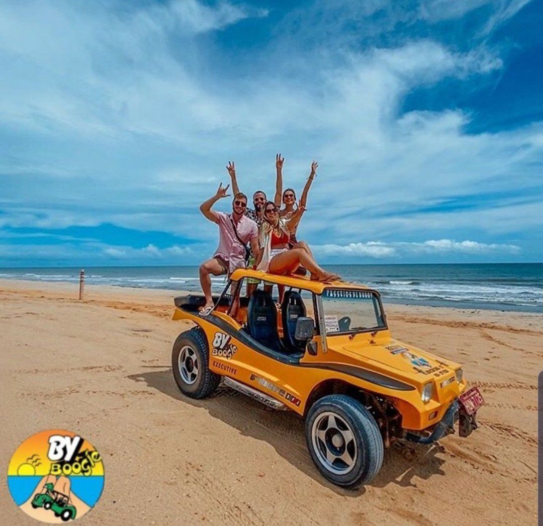 Um grupo de pessoas está posando para uma foto em um buggy amarelo na praia.