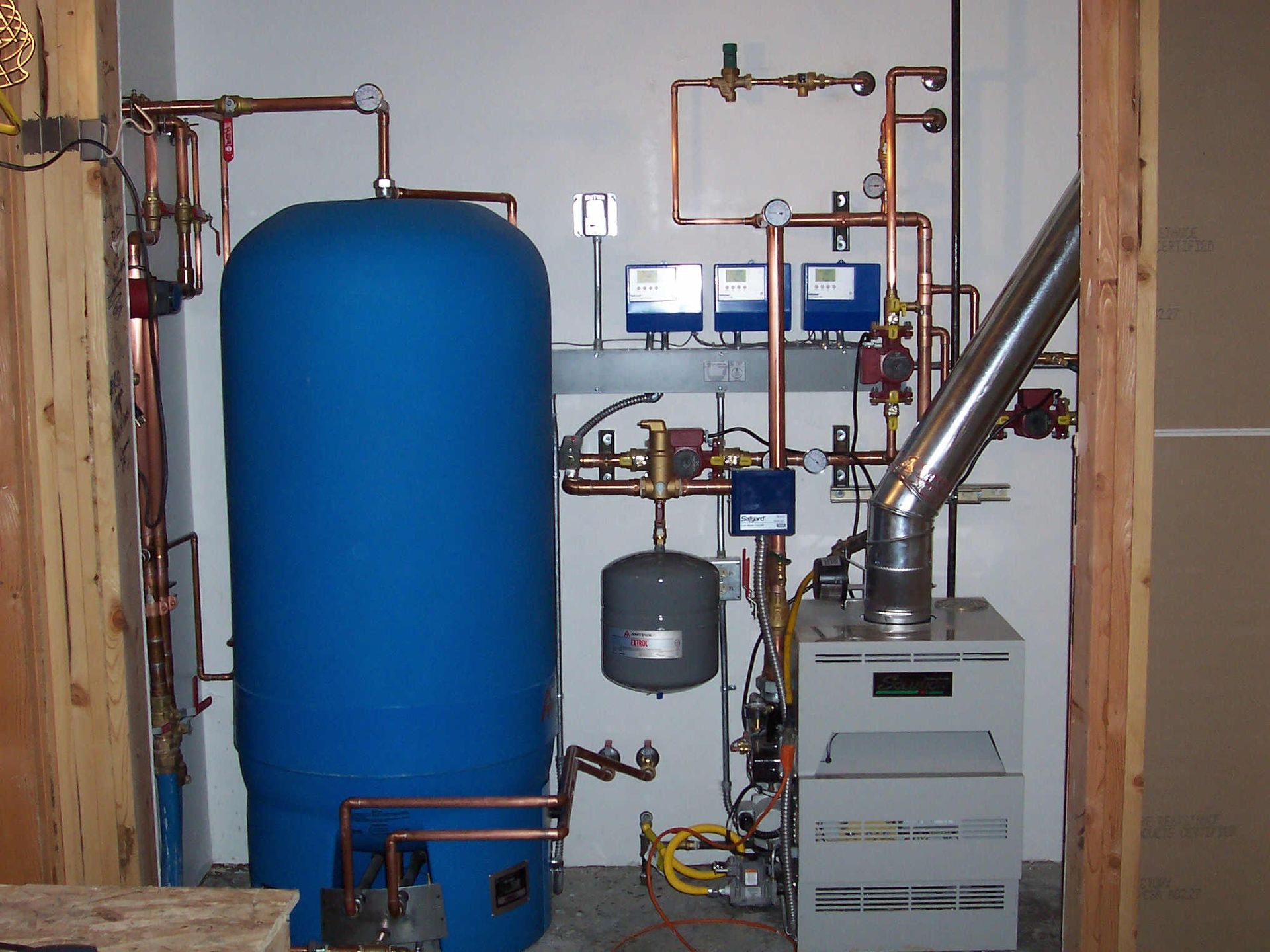 Utility room with large blue tank, pipes, gauges, and furnace equipment