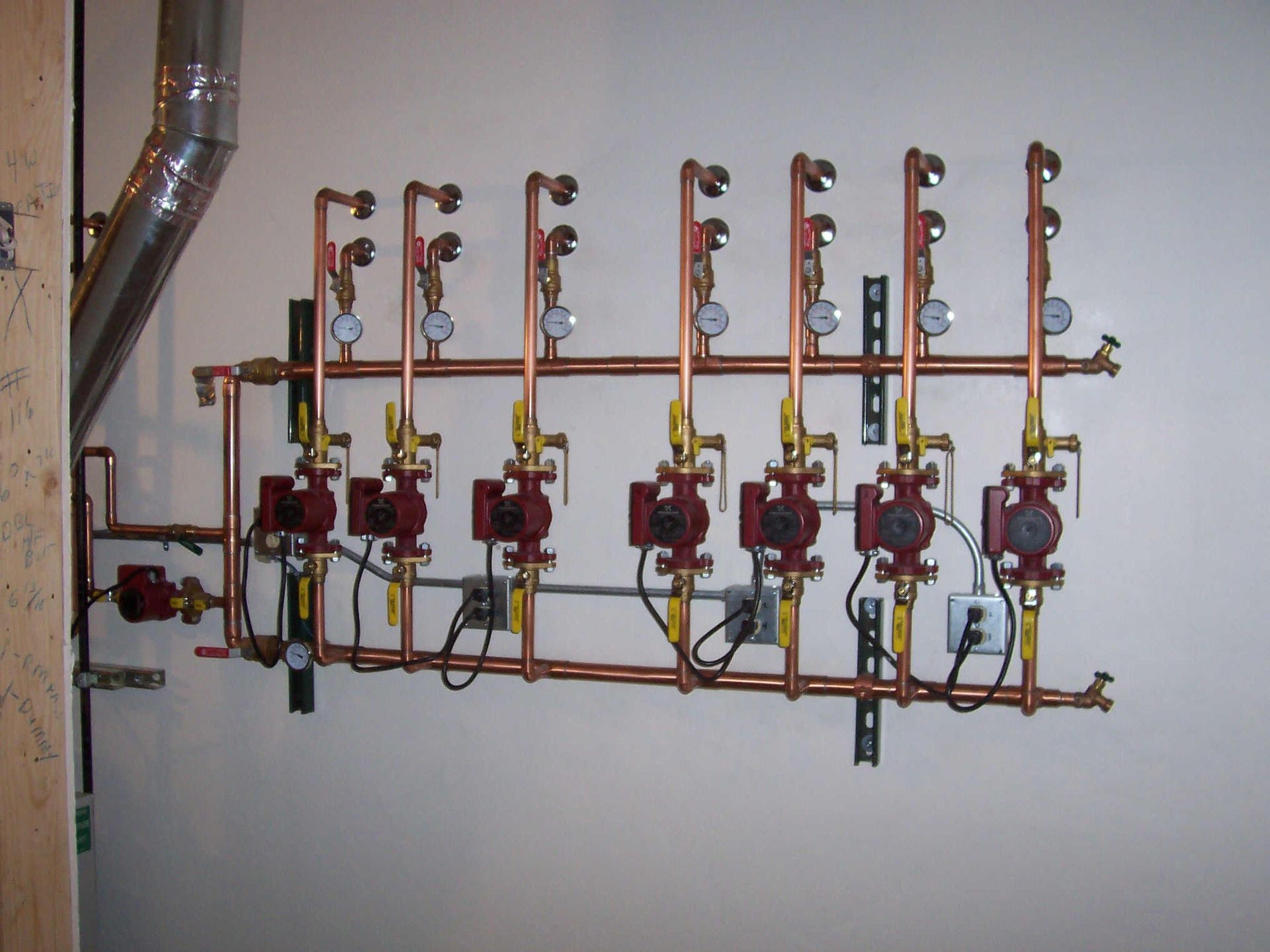 Wall-mounted plumbing manifold with red valves and yellow pipes in a utility room