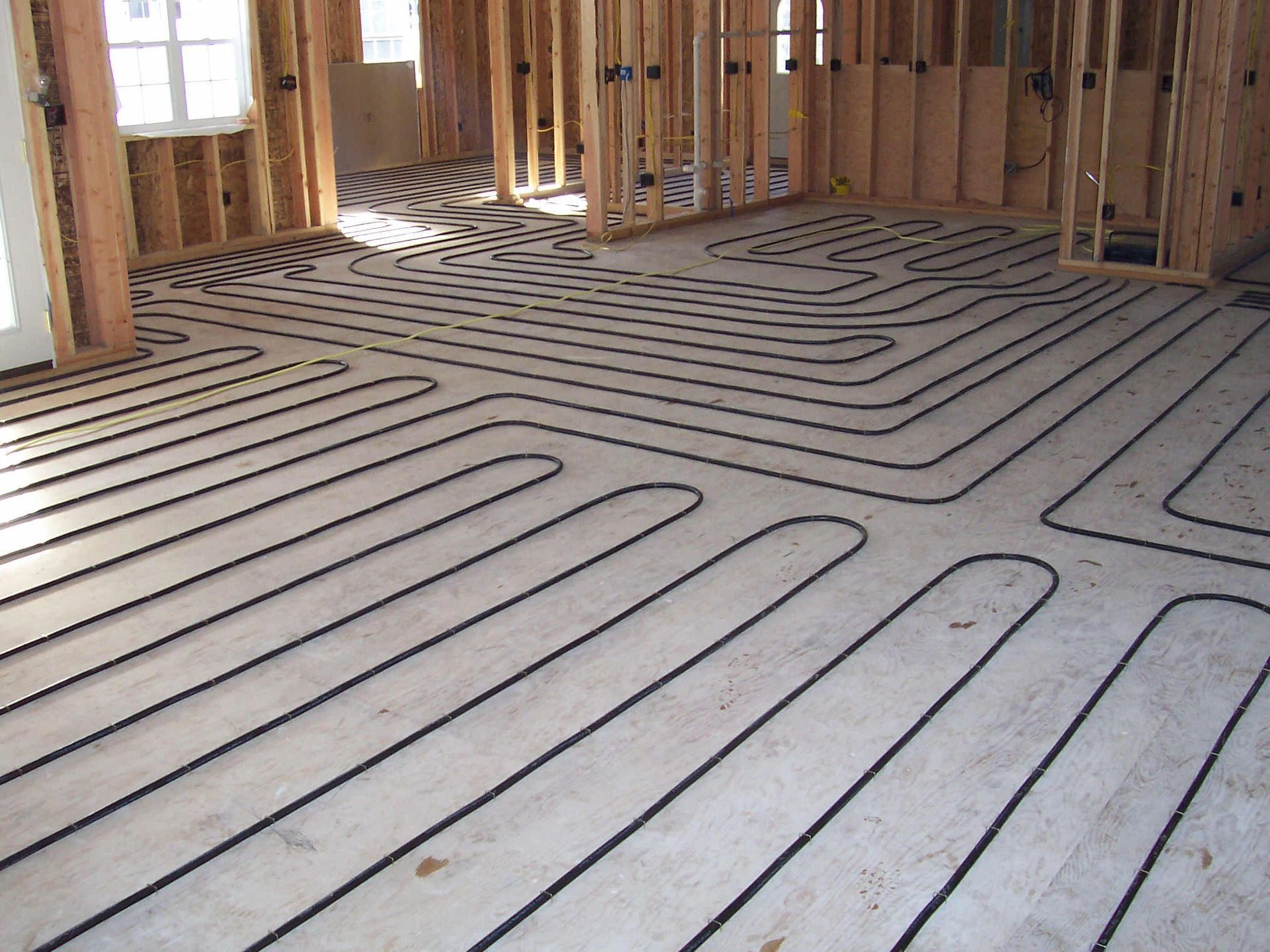Wood-framed room with underfloor heating pipes laid over a gray subfloor.