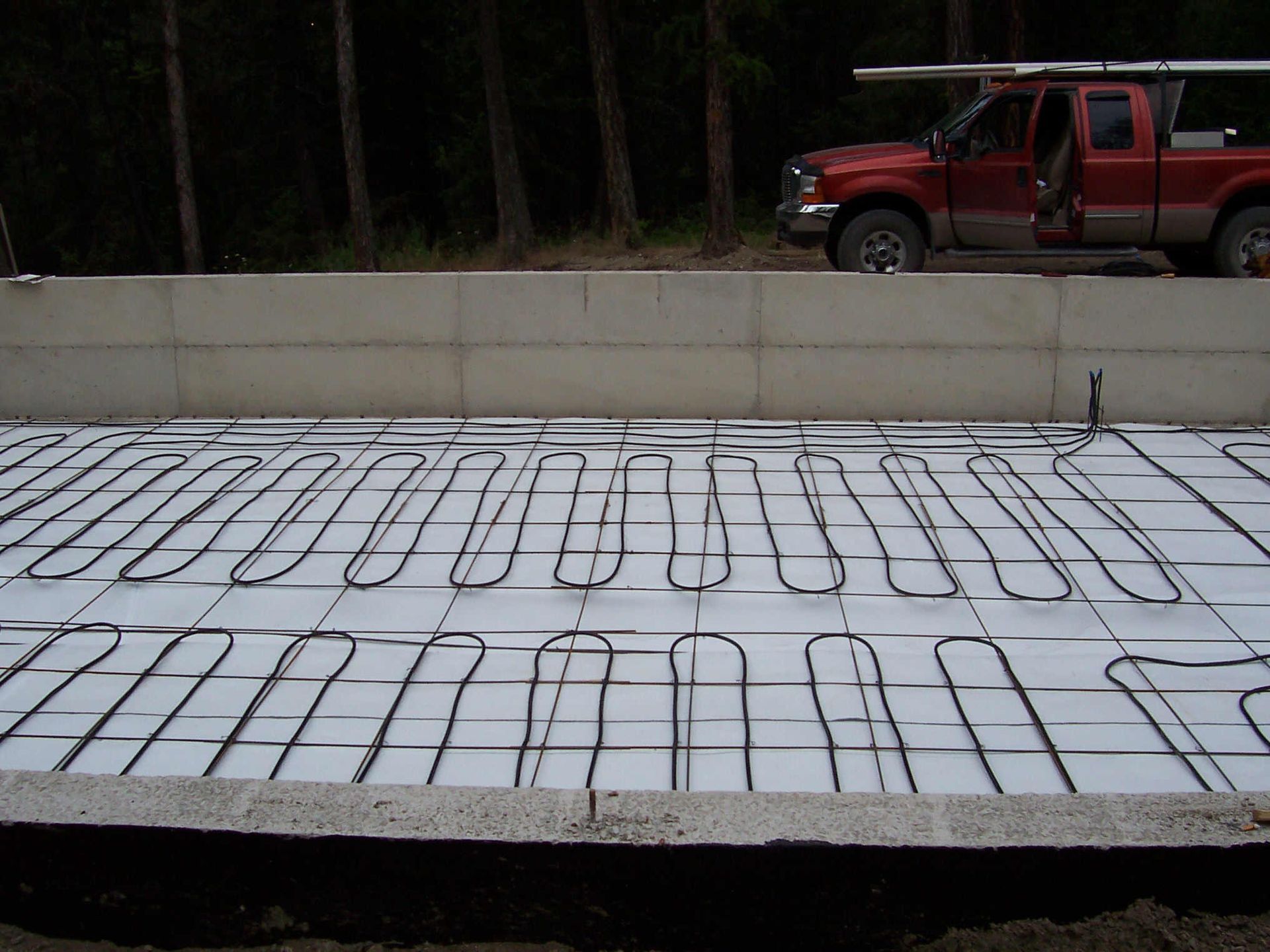 Concrete slab with exposed rebar on a construction site, with a red pickup truck in the background.