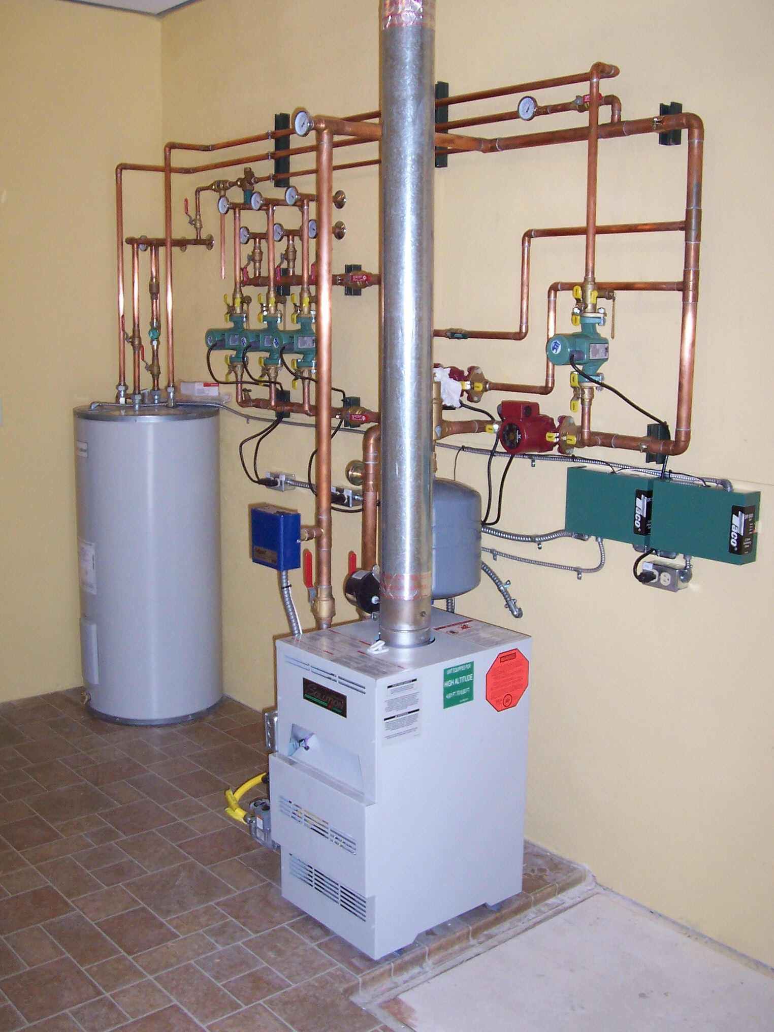 Industrial boiler and piping setup with gray tank, copper pipes, and white control unit in a utility room