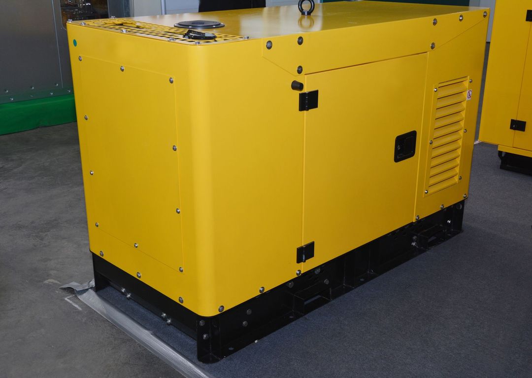 Un generatore industriale giallo, racchiuso in un involucro metallico con base nera, poggiato su un pavimento di cemento grigio.