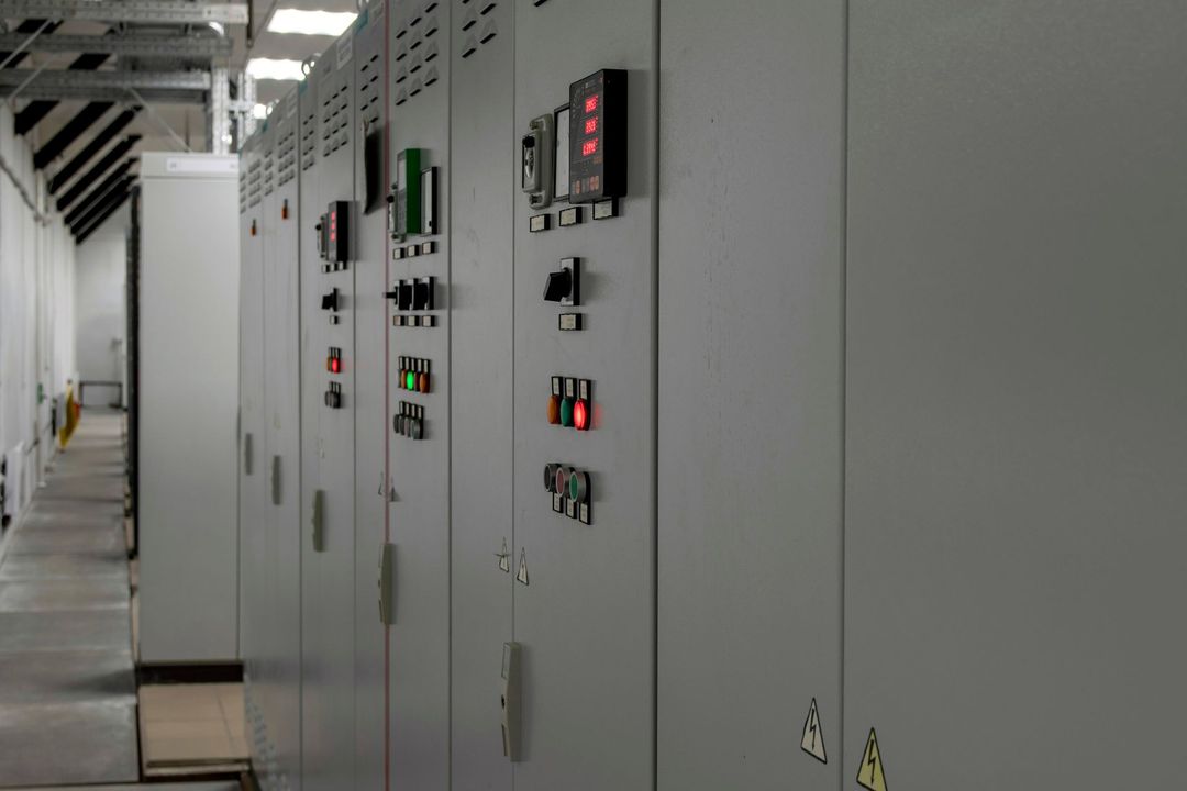 Un tecnico con elmetto e uniforme ispeziona e regola i cavi di rete collegati a un dispositivo all'interno di un quadro elettrico.