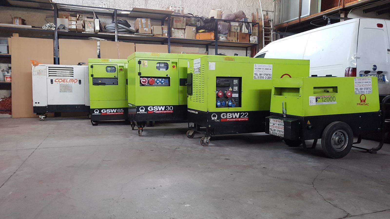 Quattro generatori industriali verde lime e un generatore bianco parcheggiati in un magazzino.