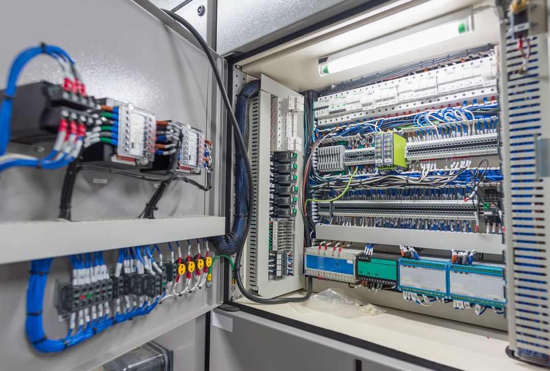 Quadro di controllo industriale aperto con cablaggio blu organizzato, morsettiere e moduli elettronici montati all'interno di un armadio.