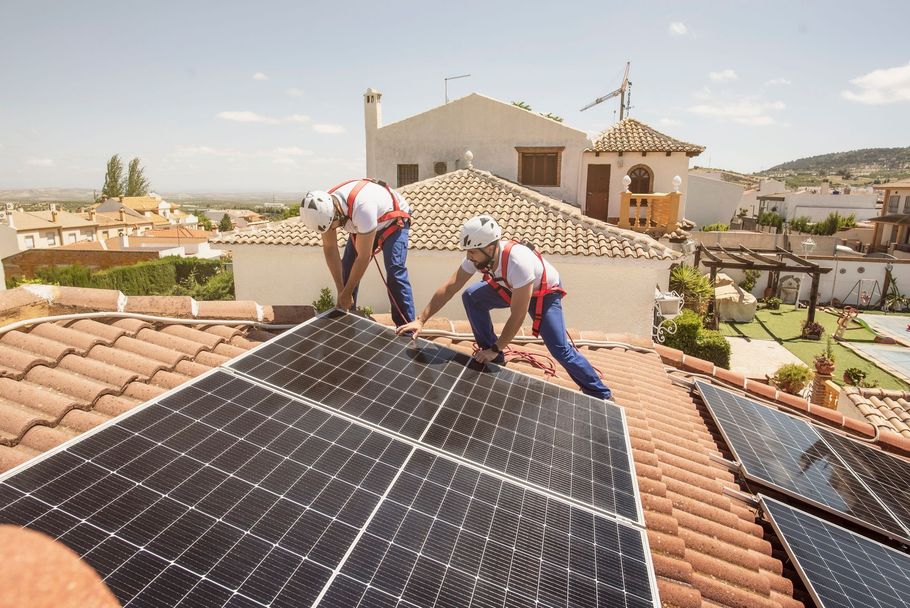 In una giornata di sole, due tecnici con caschi e imbracature installano pannelli solari sul tetto di tegole di un'abitazione.