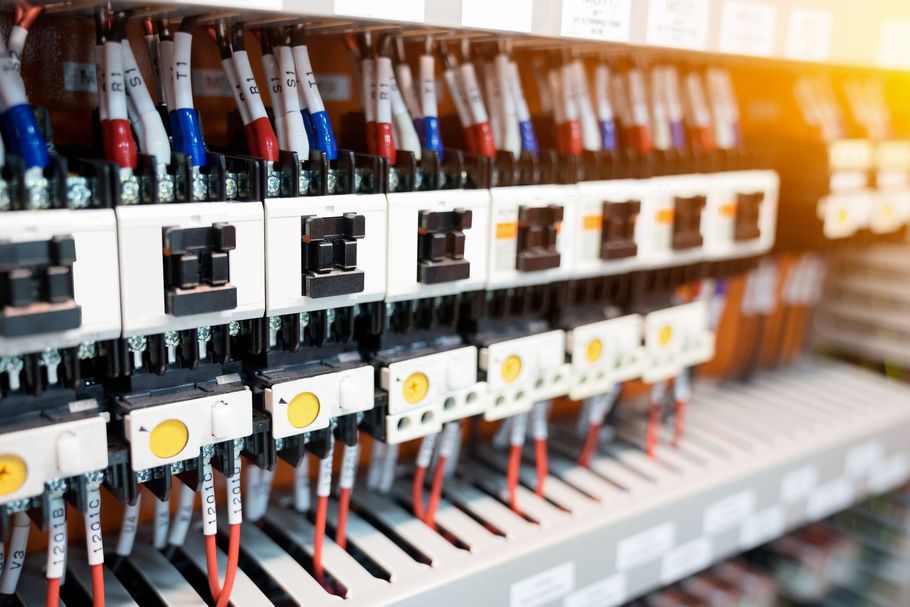 Una fila di contattori elettrici industriali montati su una guida DIN, con numerosi fili codificati a colori ed etichette bianche.