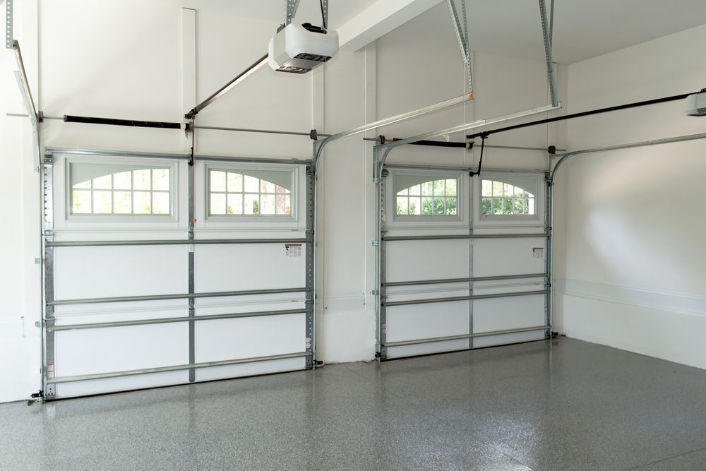 Two white sectional garage doors with arched windows installed in a garage with a grey speckled floor — Western Epoxy Works In Mudgee, NSW