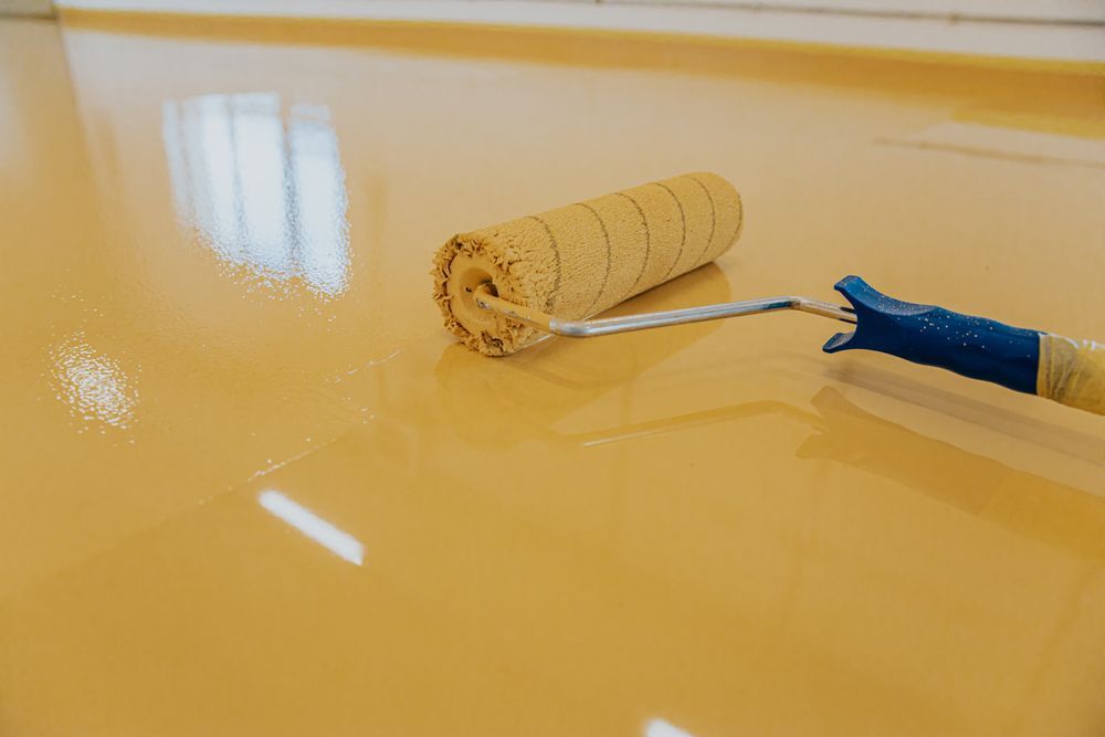 Paint Roller Resting on a Smooth, Freshly Applied Glossy Yellow Epoxy Floor Coating — Western Epoxy Works In Mudgee, NSW