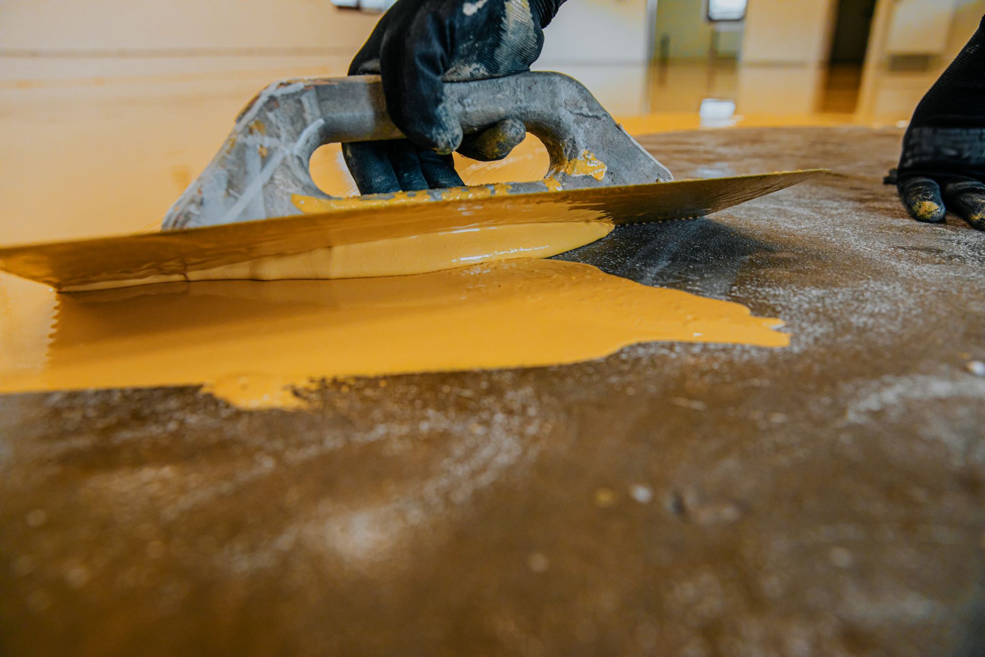 Person Uses a Metal Trowel to Spread Thick Yellow Epoxy Coating — Western Epoxy Works In Narromine, NSW