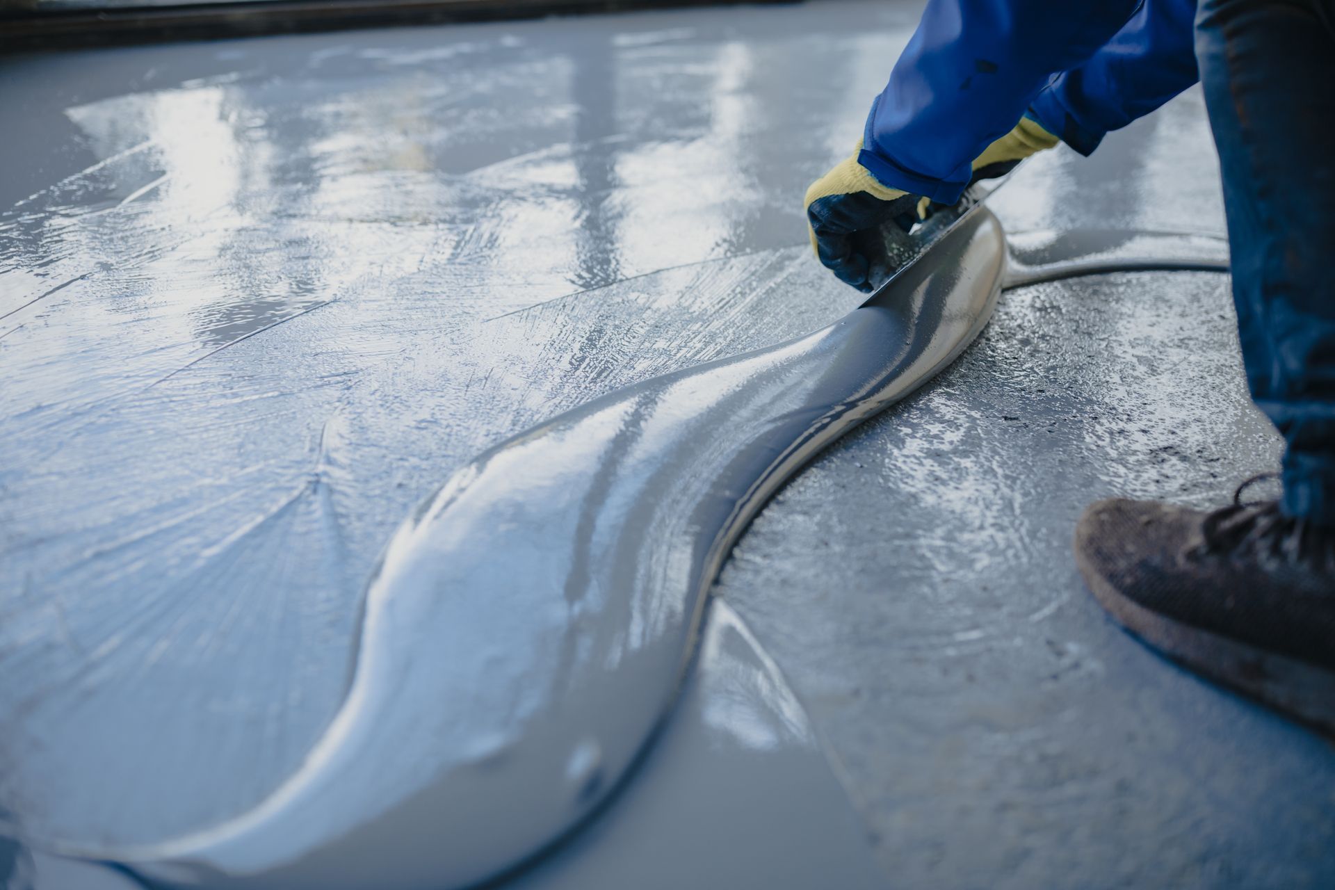 A Worker in Work Gloves Spreads Grey Epoxy Resin Across a Floor Using a Tool — Western Epoxy Works In Narromine, NSW