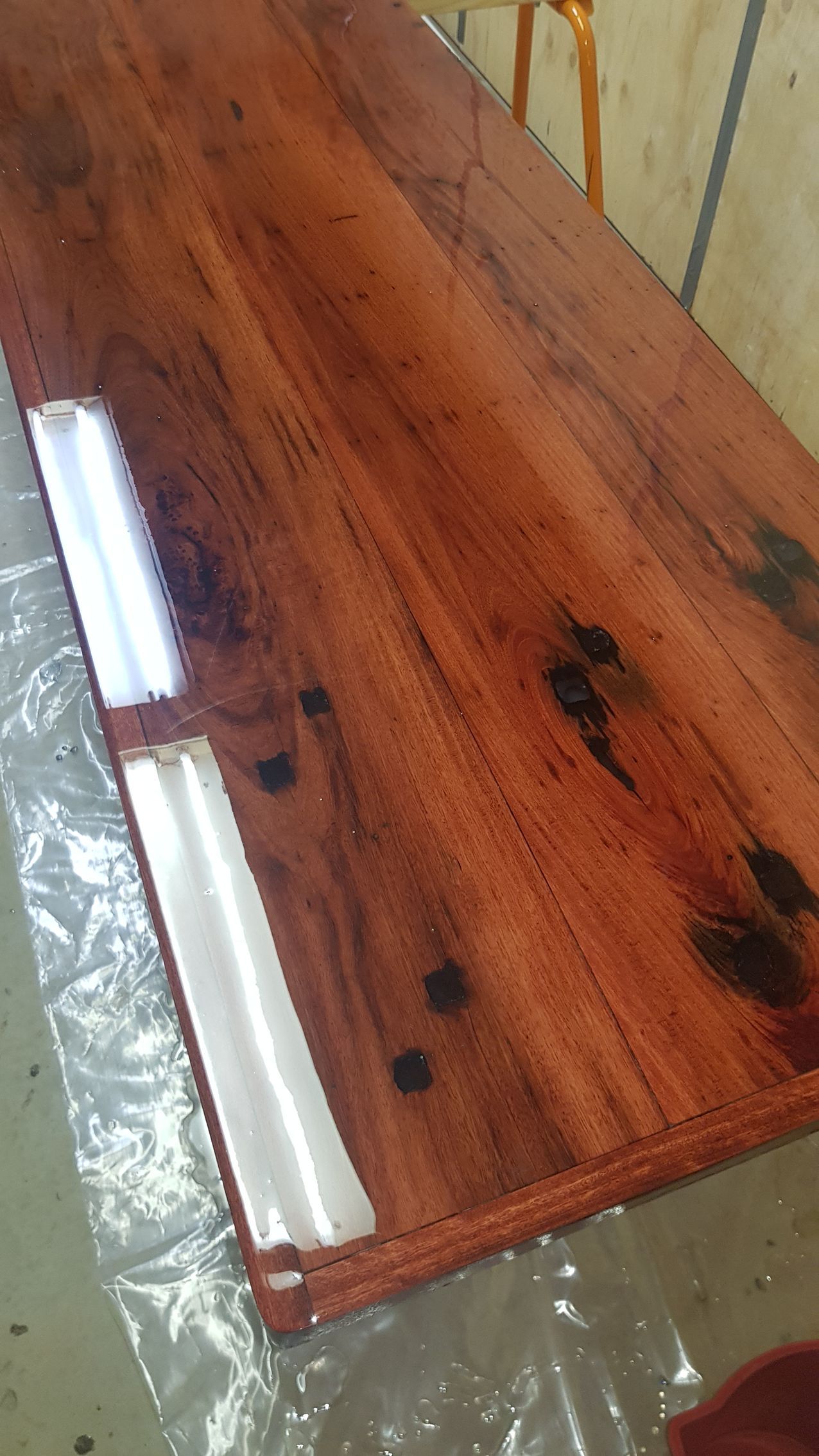 Wooden tabletop with glossy finish and two white handles on a plastic-covered surface