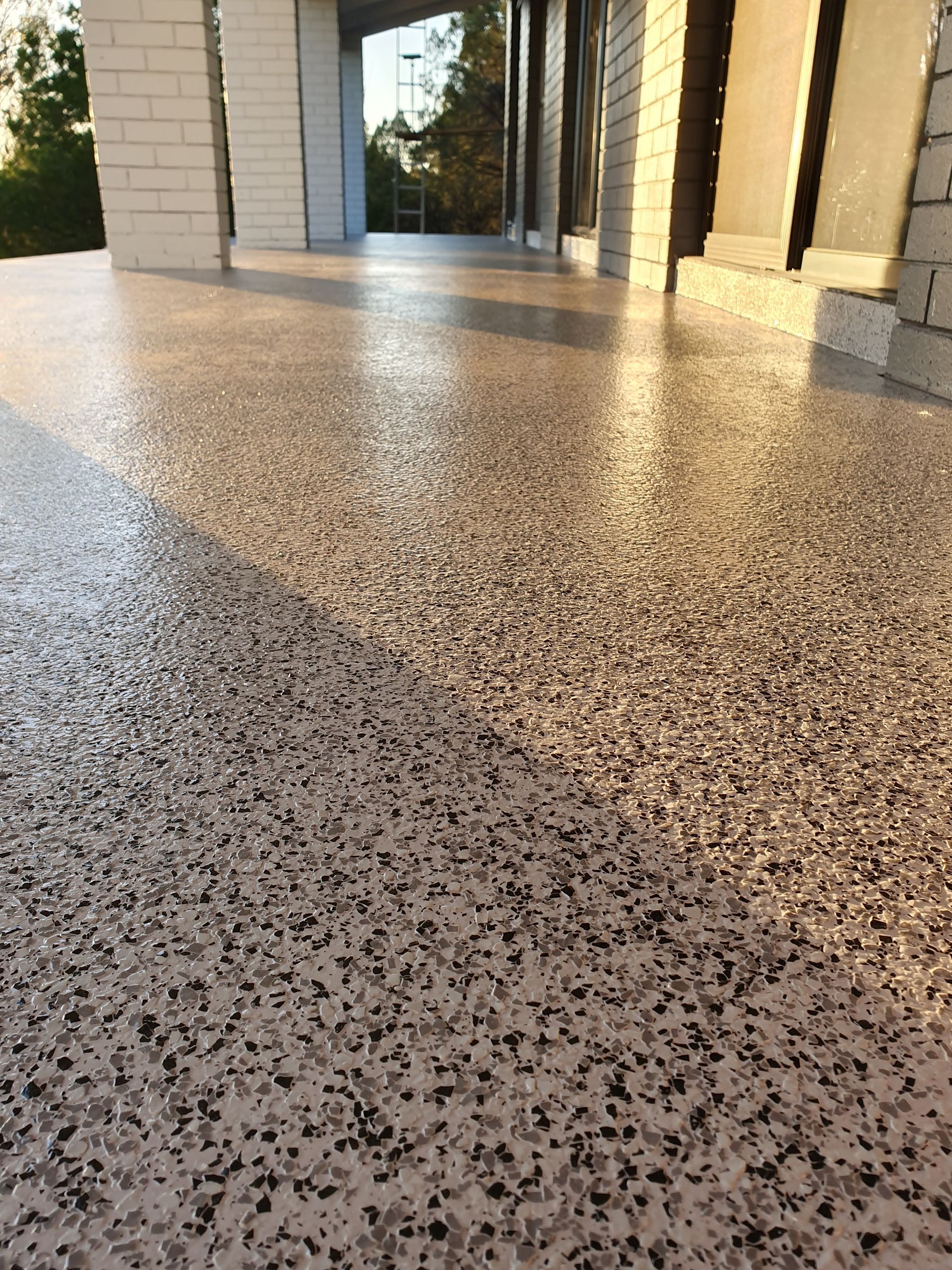 Speckled terrazzo floor beside a building entrance with glass doors and sunlight reflections