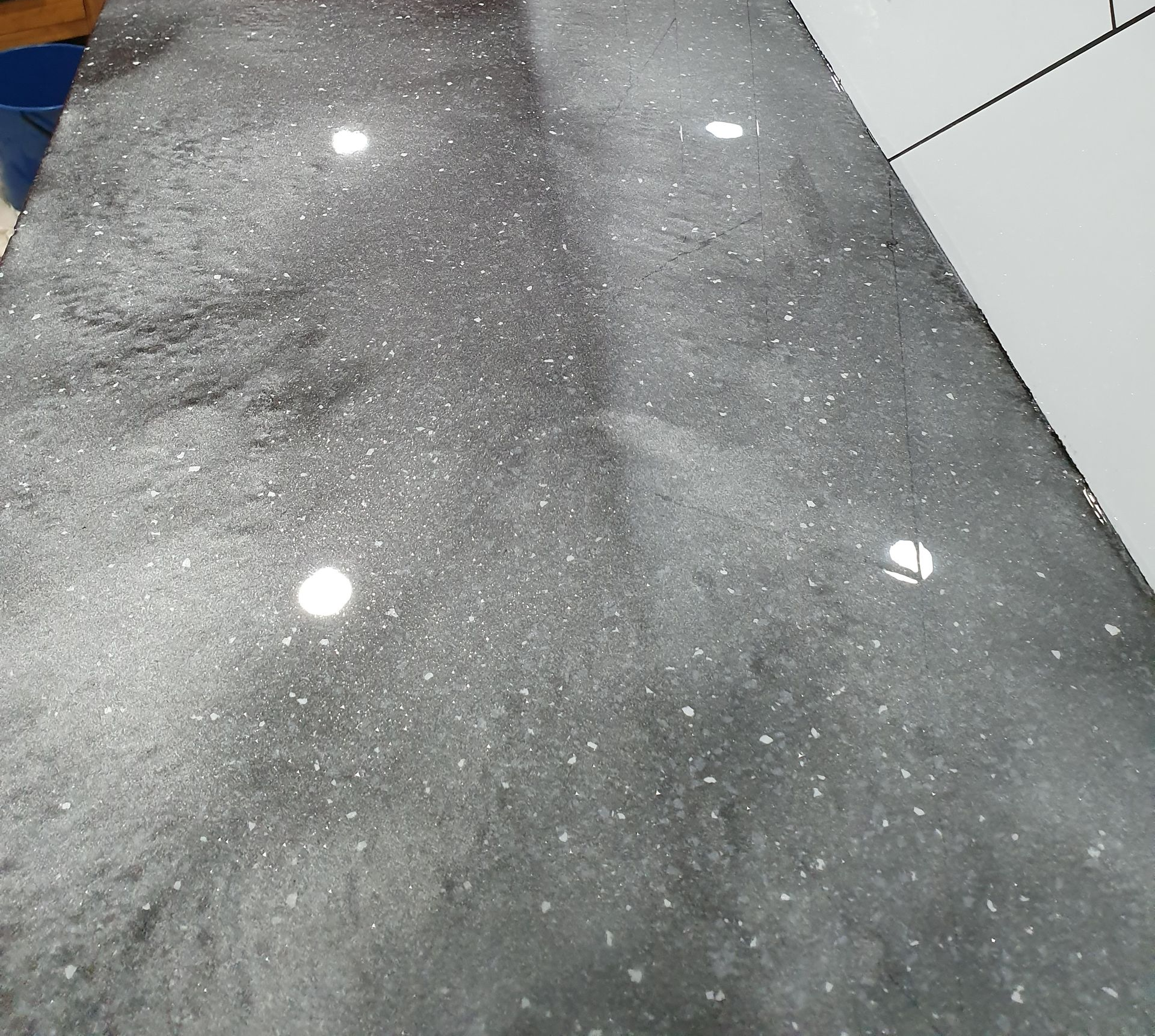 Gray speckled stone countertop with reflected ceiling lights in a tiled room