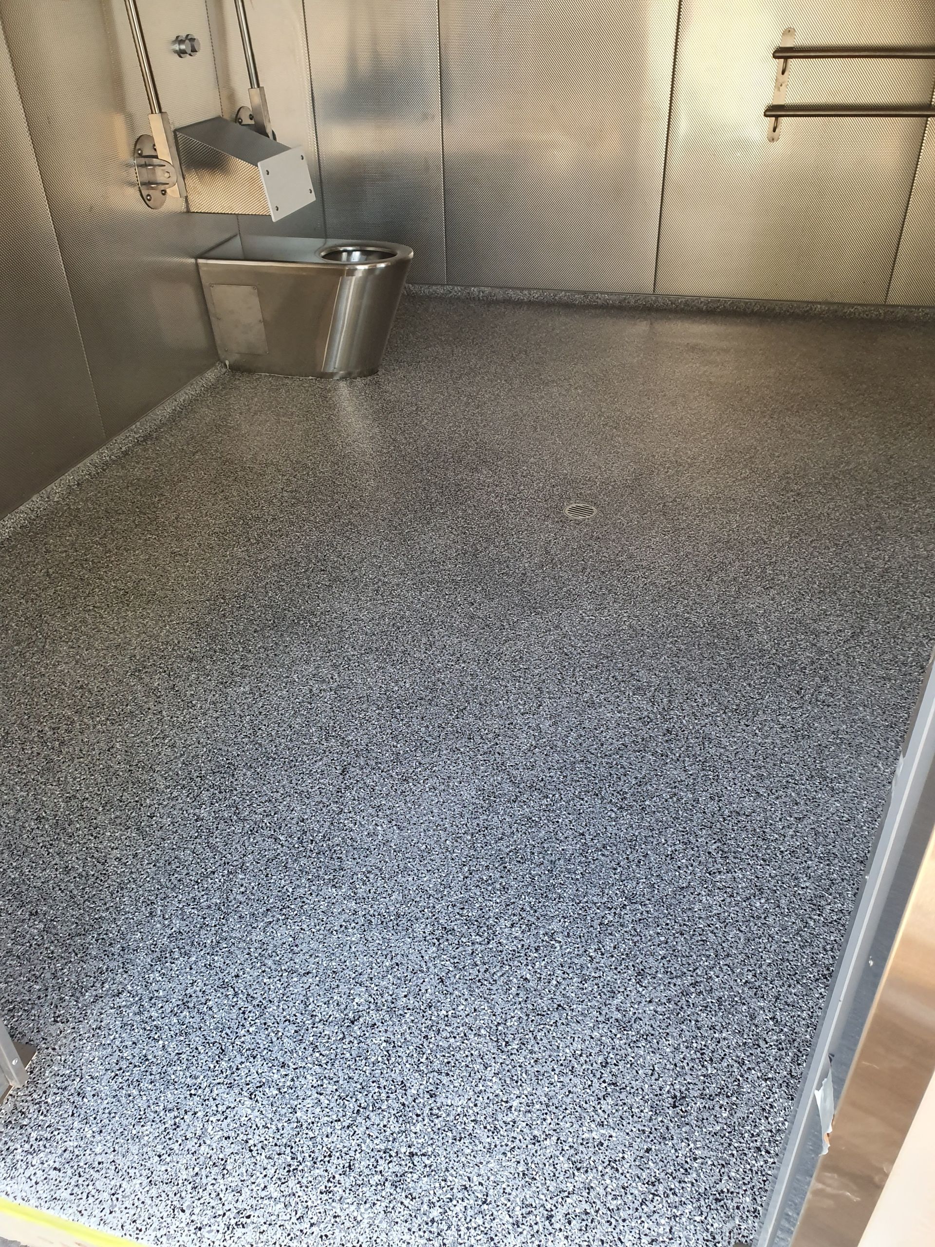 Small indoor room with speckled gray floor and corrugated metal walls, plus a metal bin in the corner
