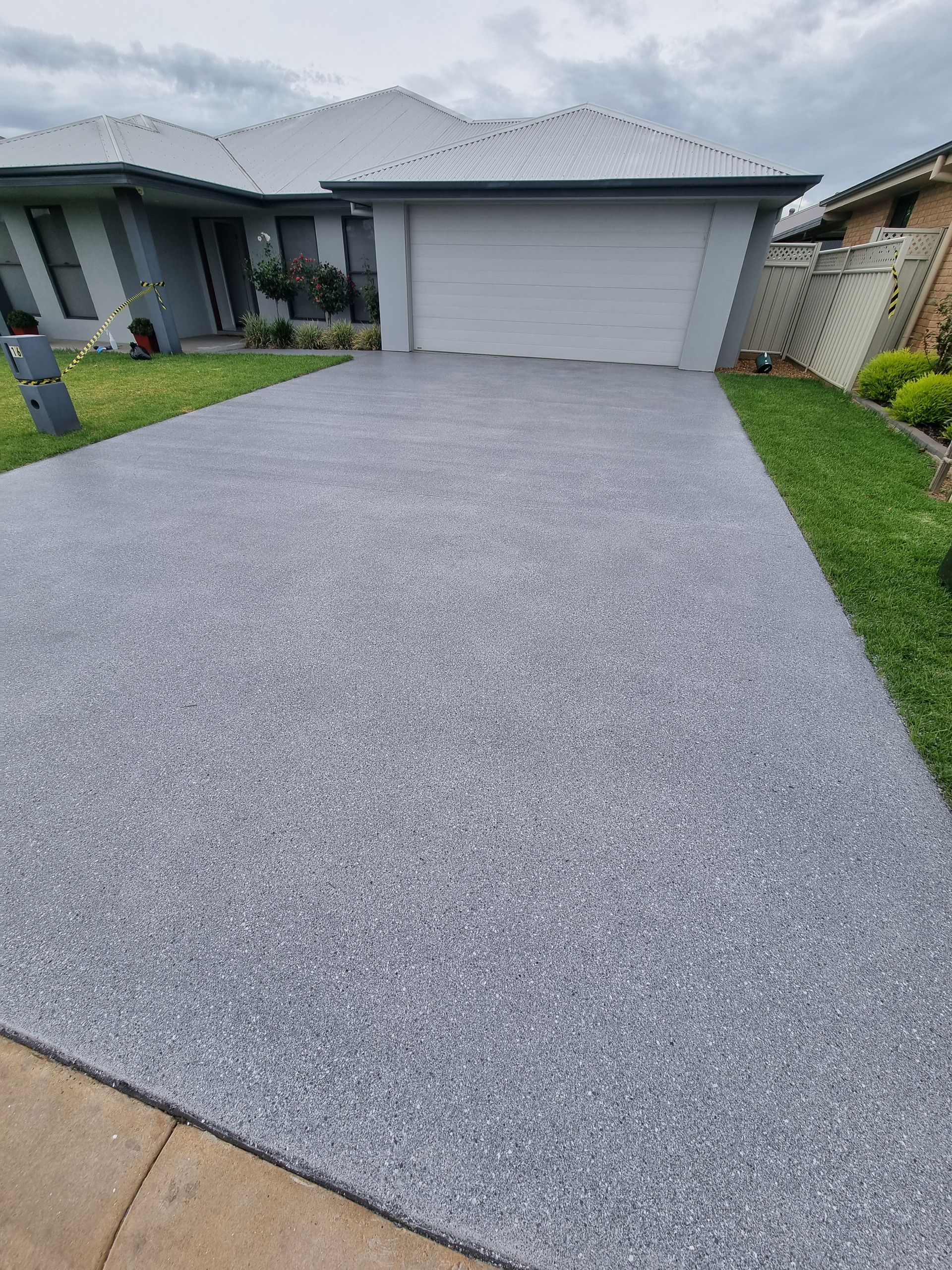 Freshly coated gray driveway leading to a garage in a suburban house exterior