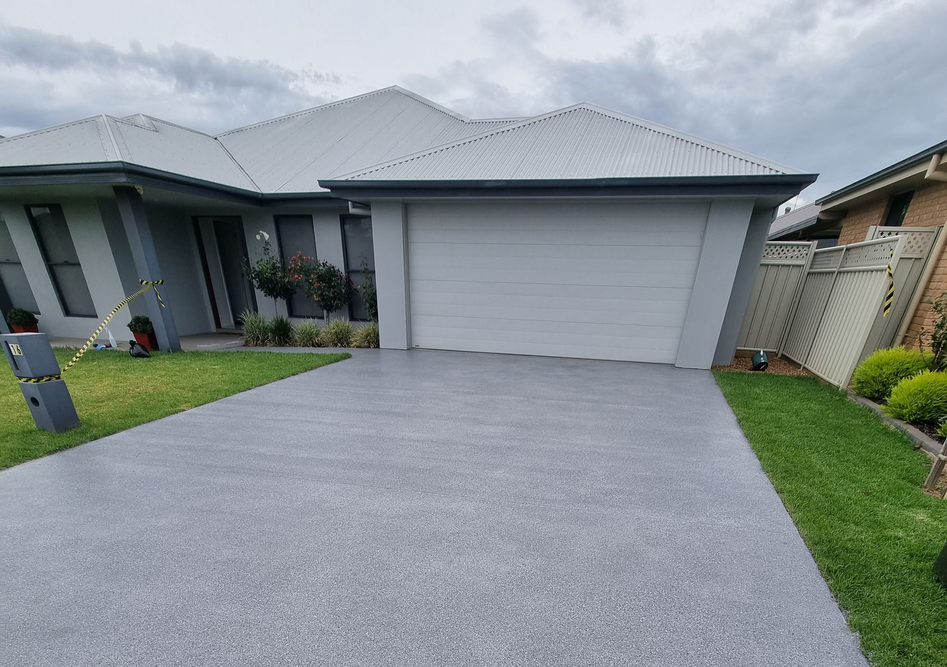 Modern house with a gray driveway, two-car garage, and small green lawn under cloudy skies