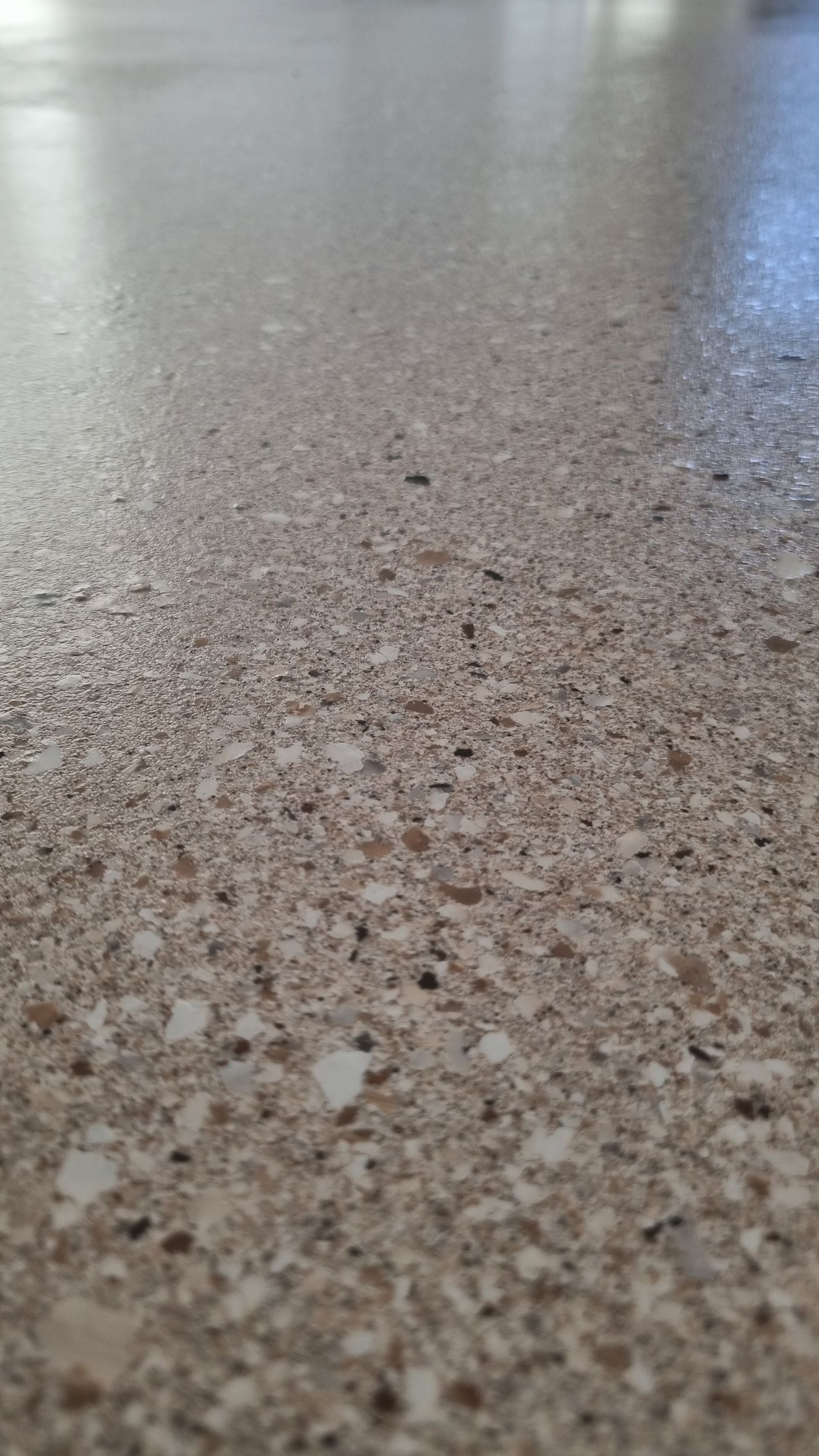 Close-up of a speckled stone or terrazzo floor with a blurred light reflection in the background
