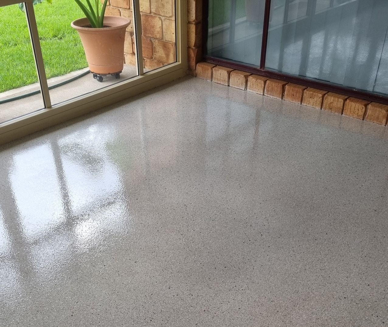 Reflective speckled terrazzo floor near a window, with a potted plant in the corner